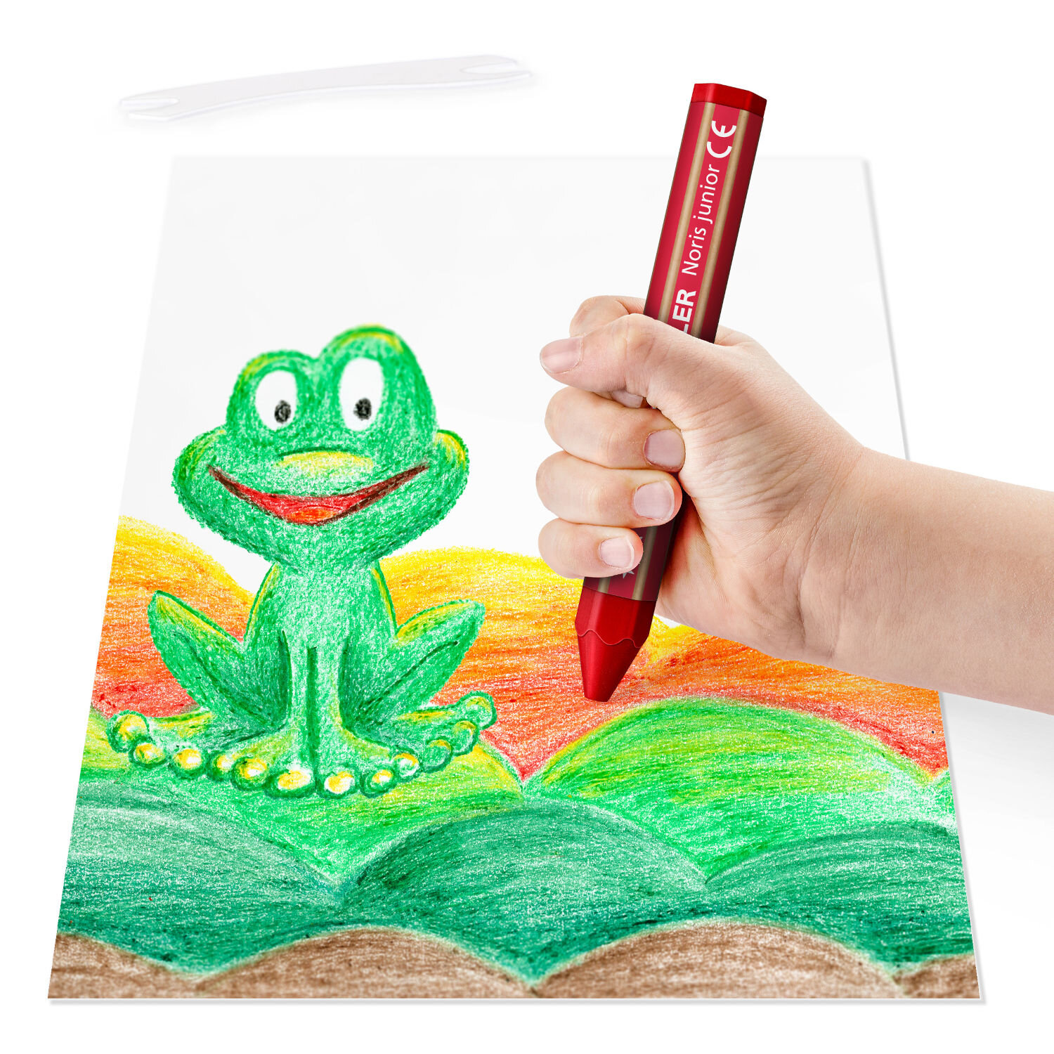 Noris Junior Wachsmalkreide Set 6 Stück zeigt eine Kinderhand, die mit einem Staedtler Wachsmalstift einen bunten Frosch auf Papier ausmalt
