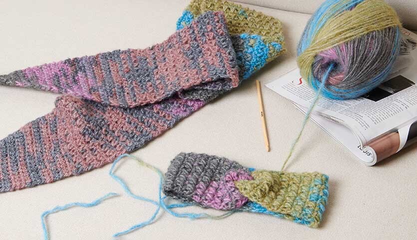 Häkelanleitung Stirnband und Tuch aus Creative Painted Power: Bunte Wolle, Häkelnadel und fertige Accessoires auf einem Tisch.