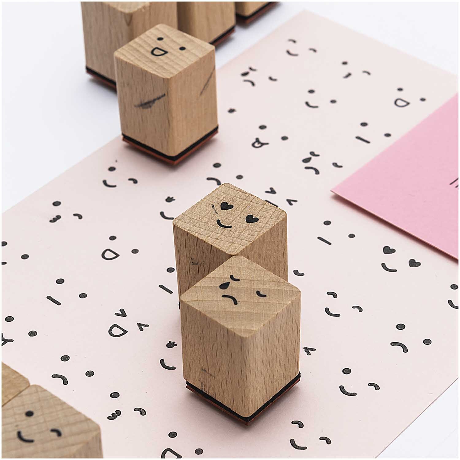 Paper Poetry Stempelset Smile, 13-teilig, zeigt Holzstempel mit verschiedenen Gesichtsausdrücken auf Papier. Ideal für kreative Bastelprojekte.