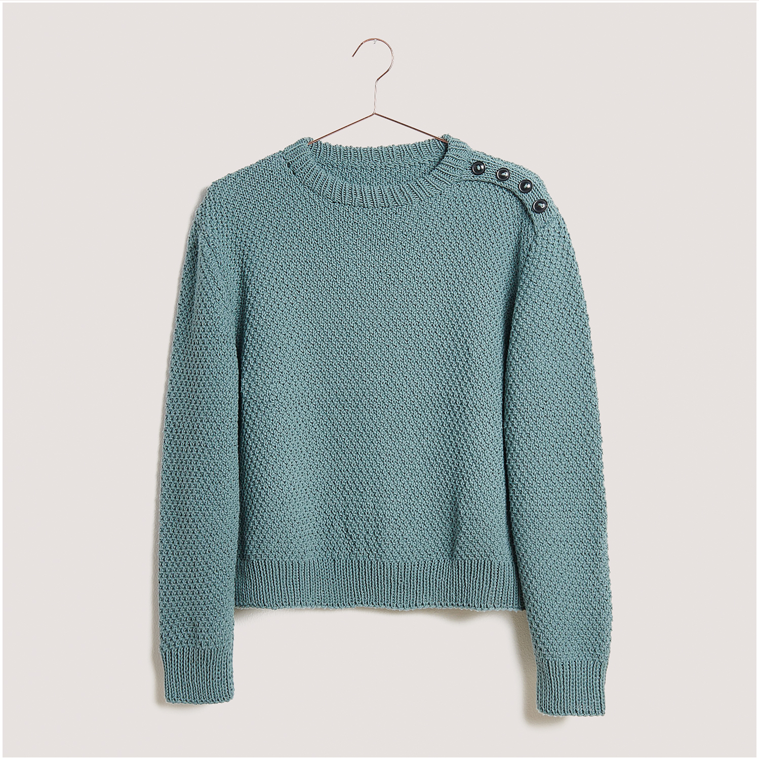 Strickset Pullover Modell 30 aus Lovewool Nr. 18 in Blau mit Knöpfen an der Schulter auf einem Kleiderbügel.
