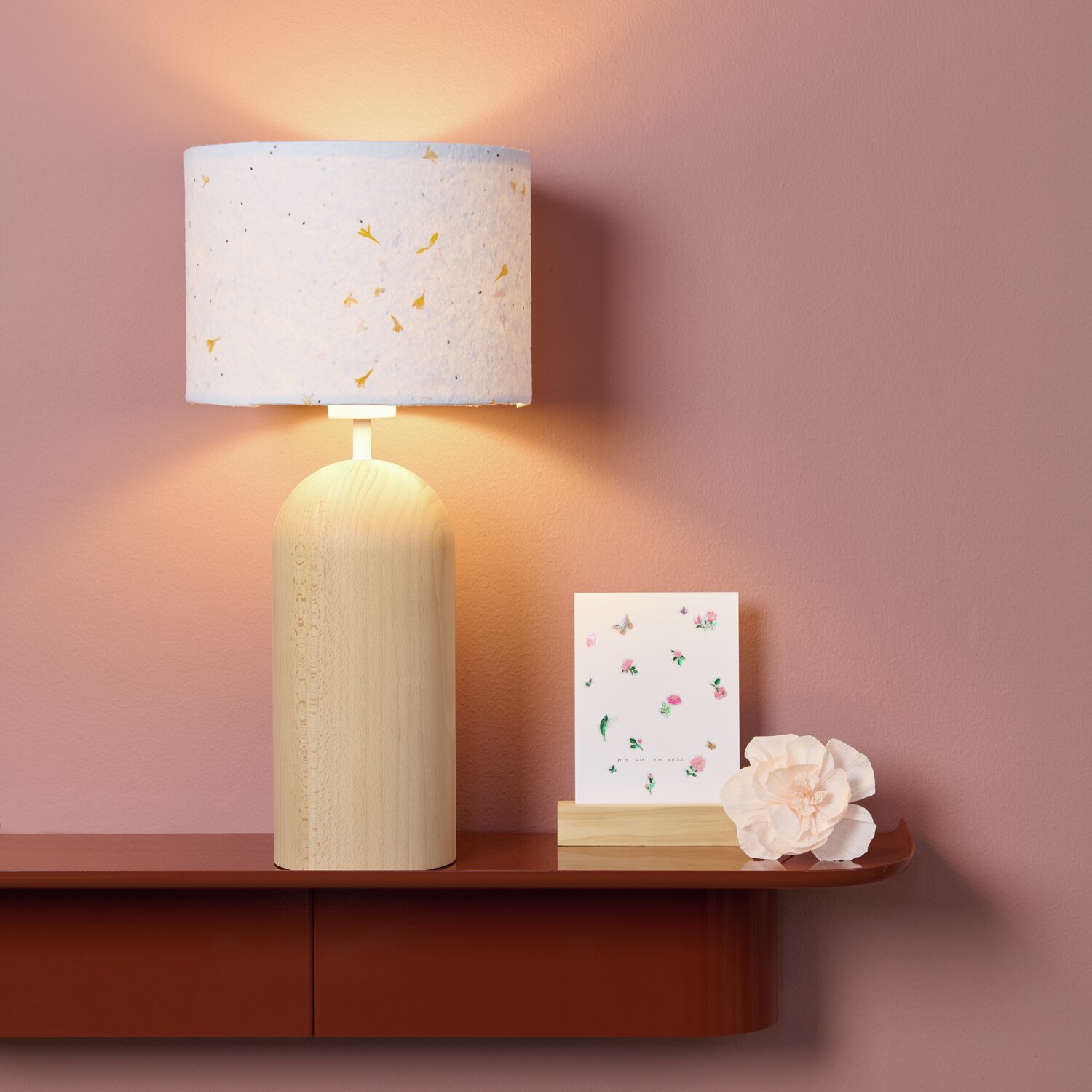 Paper Poetry Bastelbogen Baumwollpapier mit Blüten, dekorativ auf einem Regal neben einer Lampe und einer Blume arrangiert.
