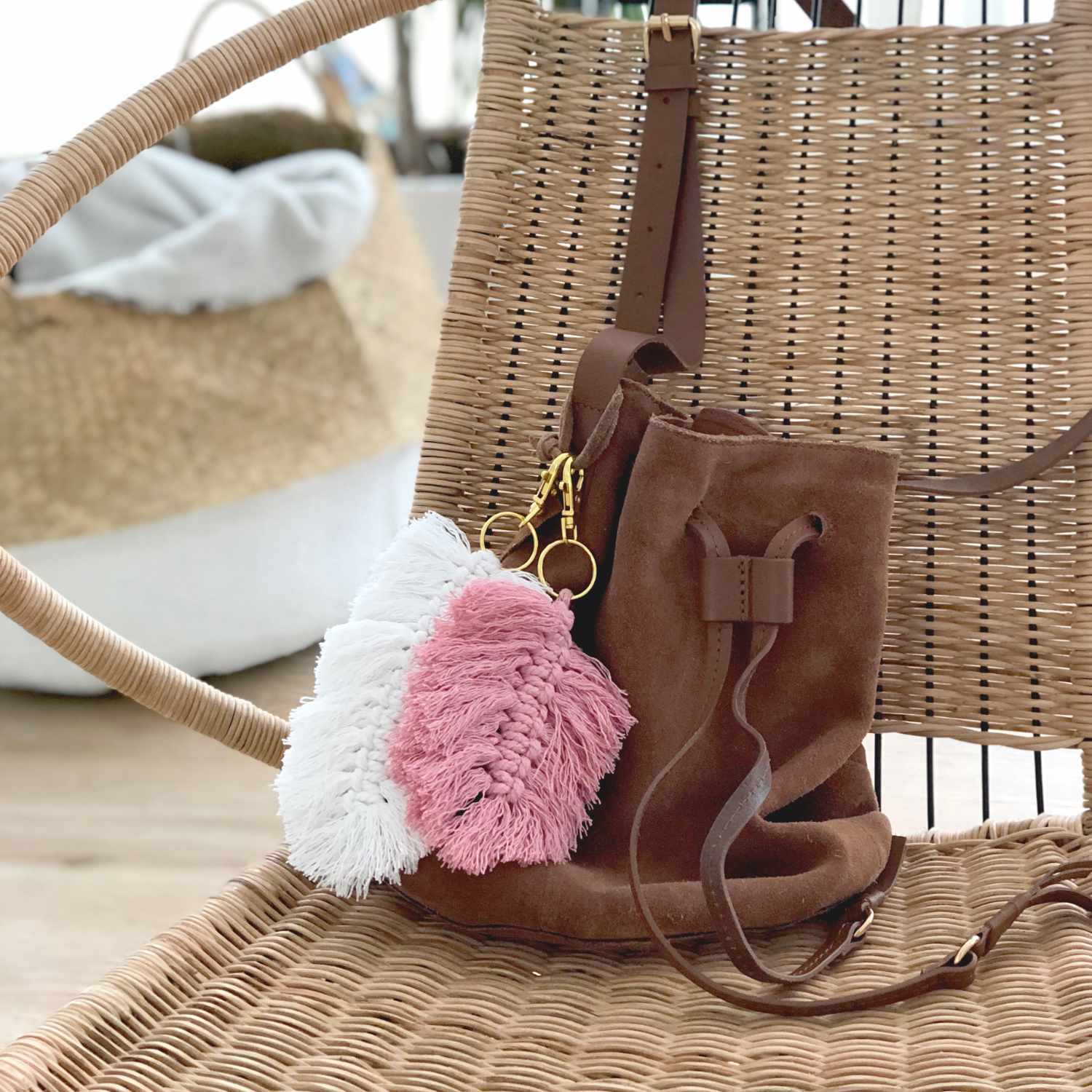 Anleitung Makramee-Federanhänger knüpfen: Zwei Federanhänger in Rosa und Weiß an einer braunen Tasche.