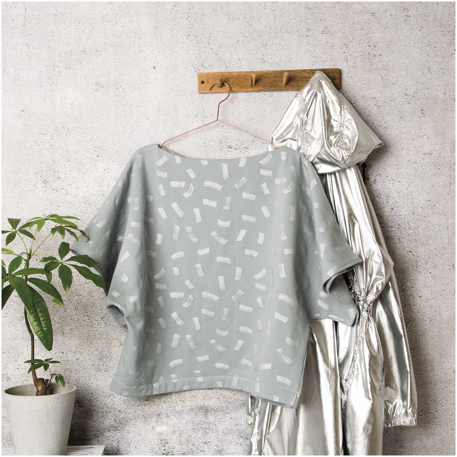 Sweatshirt-Stoff Crafted Nature Striche in einem Raum mit Pflanze und silberner Jacke auf Holzaufhänger.