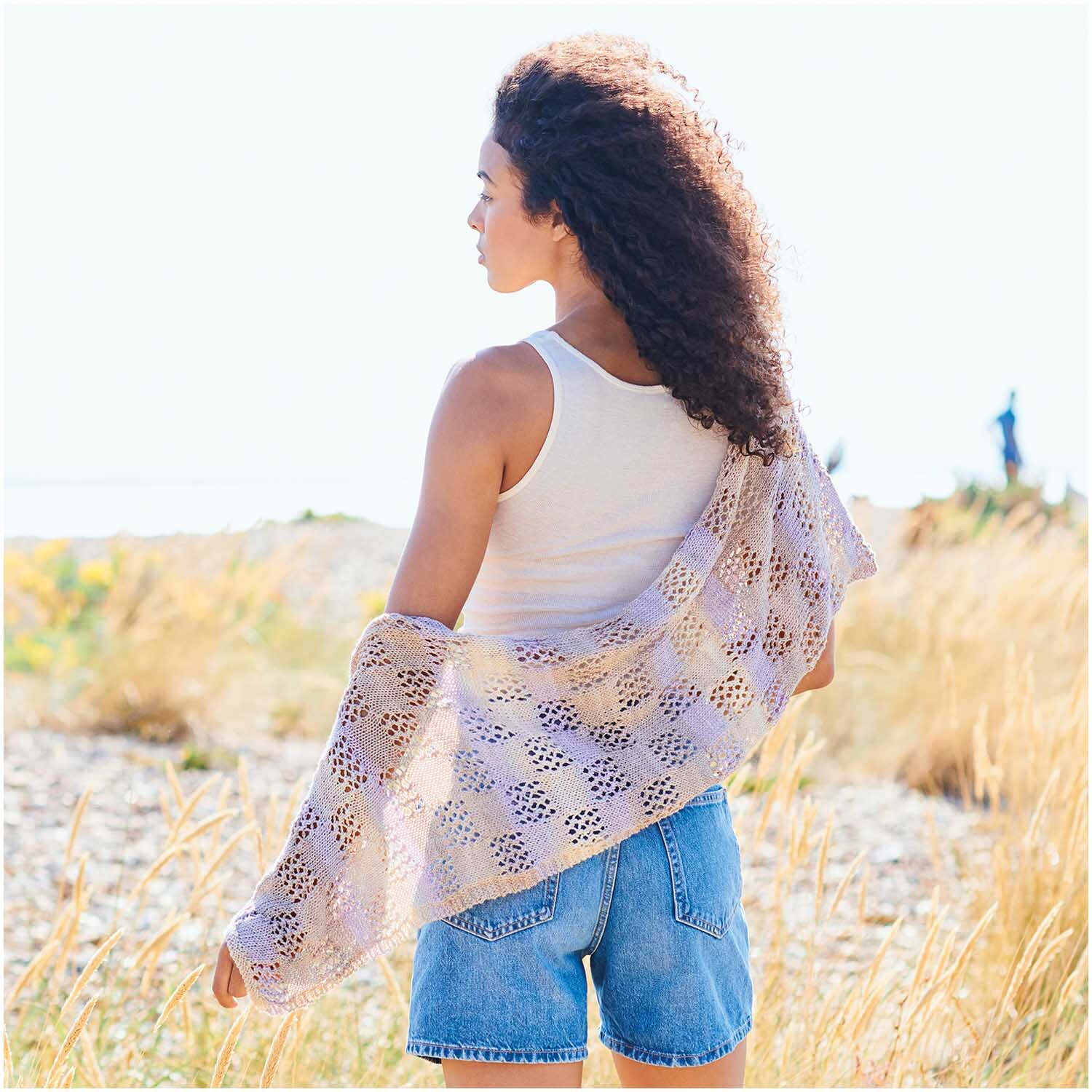 Creative Cotton Camouflage: Frau am Strand mit gehäkeltem Schal in Beige, sommerliche Atmosphäre.