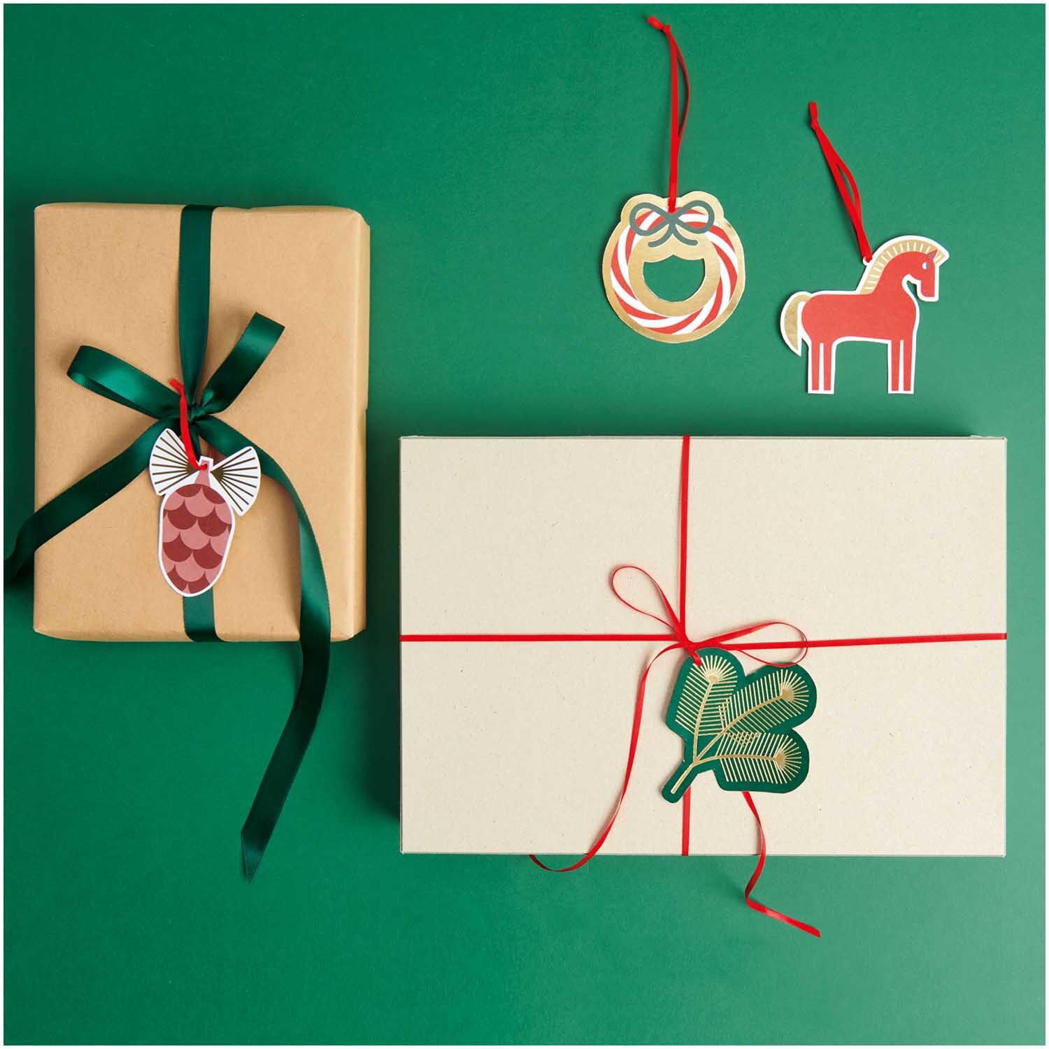 Paper Poetry Geschenkanhänger Christmas Rocks! 8 Stück von Rico Design, dekoriert auf Geschenken mit roten und grünen Bändern auf grünem Hintergrund.