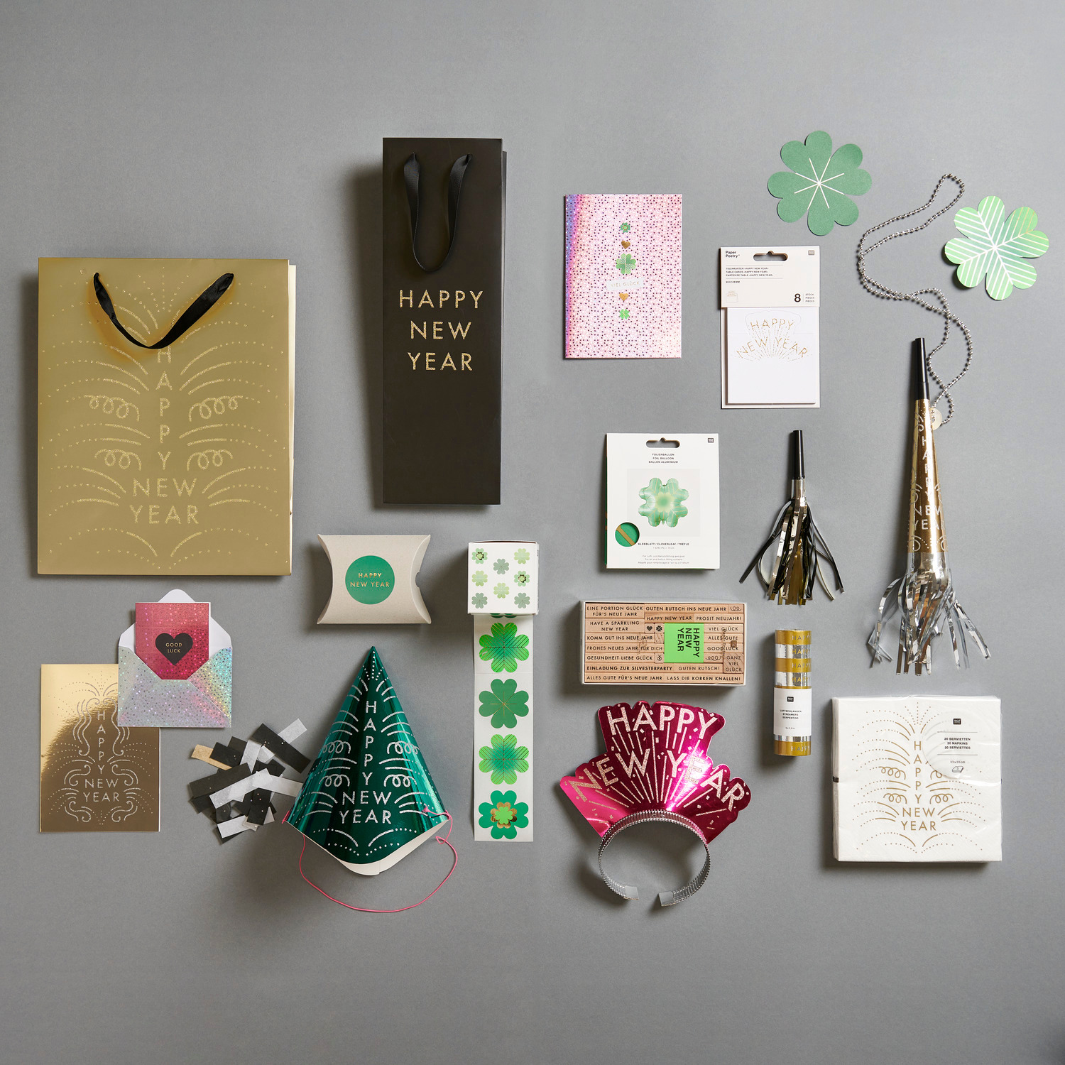 Paper Poetry Geschenktüte Happy New Year in Gold, umgeben von Partydekorationen und Glücksbringern. Ideal für festliche Anlässe.