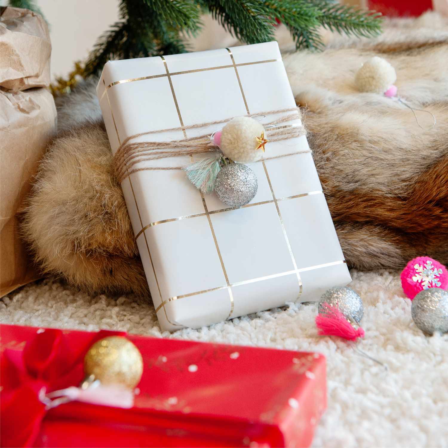 Pompon- und Kugel-Anhänger neon-pastell 6 Stück dekorieren ein Geschenk mit festlichem Flair vor einem Weihnachtsbaum.