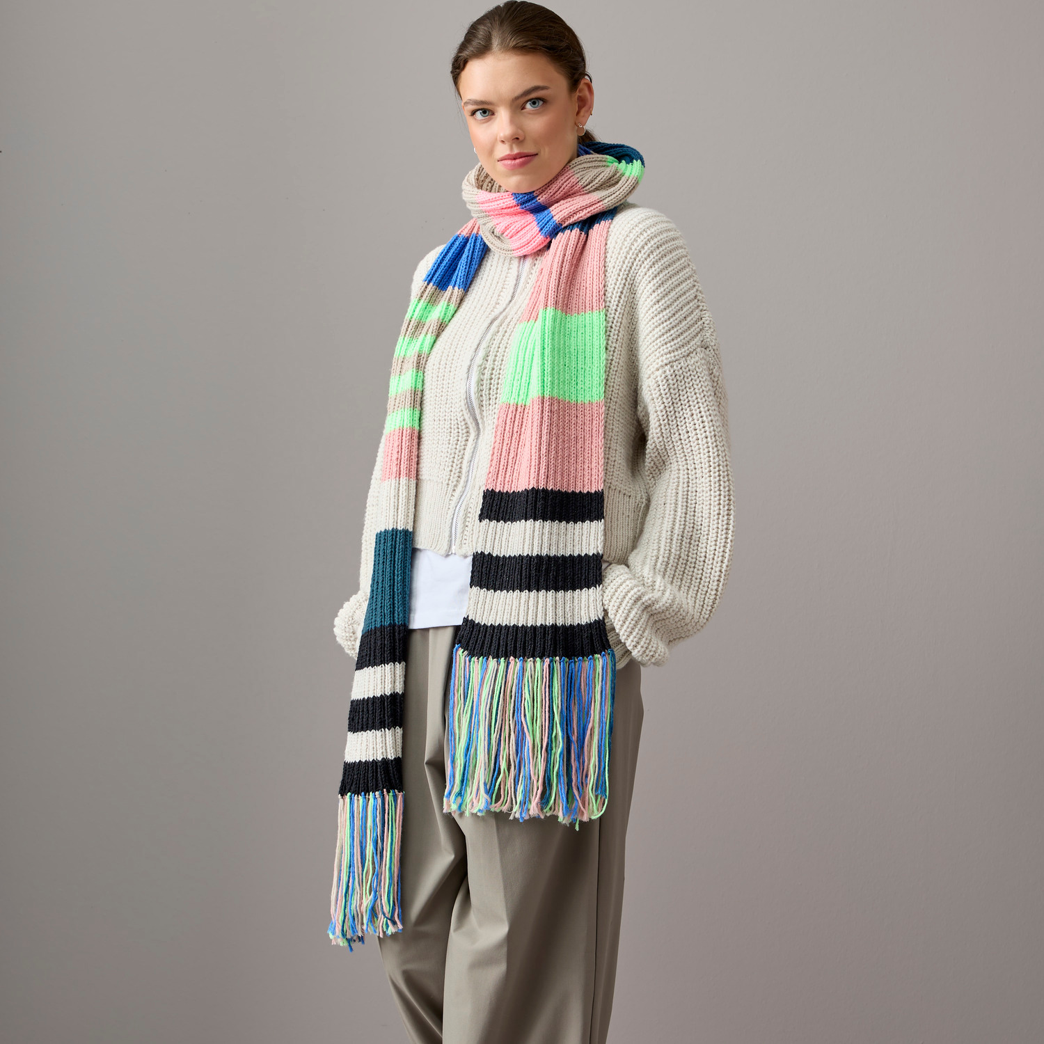 Essentials Vegan Cashmere aran: Frau trägt gestreiften Schal in Creme, Altrosa, Blau und Grün. Perfekt für stilvolle Wintermode.