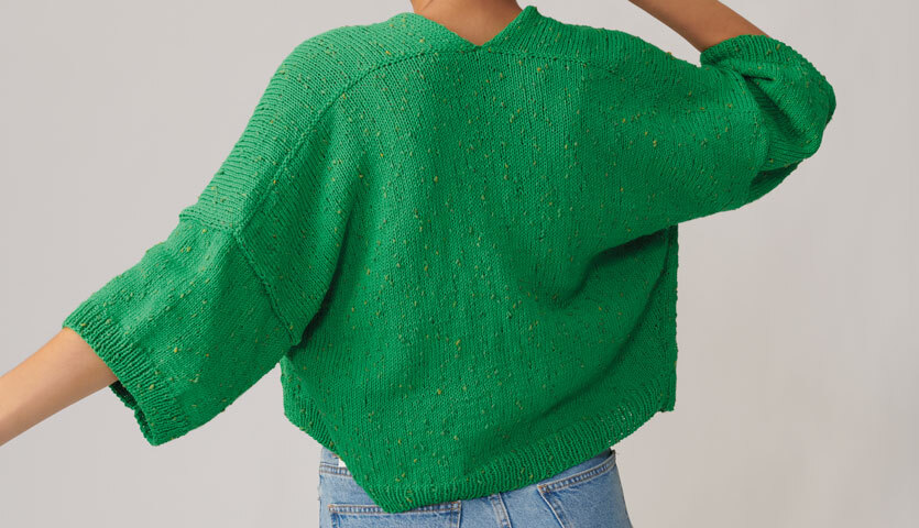 Strickanleitung Jacke aus Fashion Cotton Neps dk: Grüne Strickjacke mit Dreiviertelärmeln, getragen von Person in blauer Jeans.