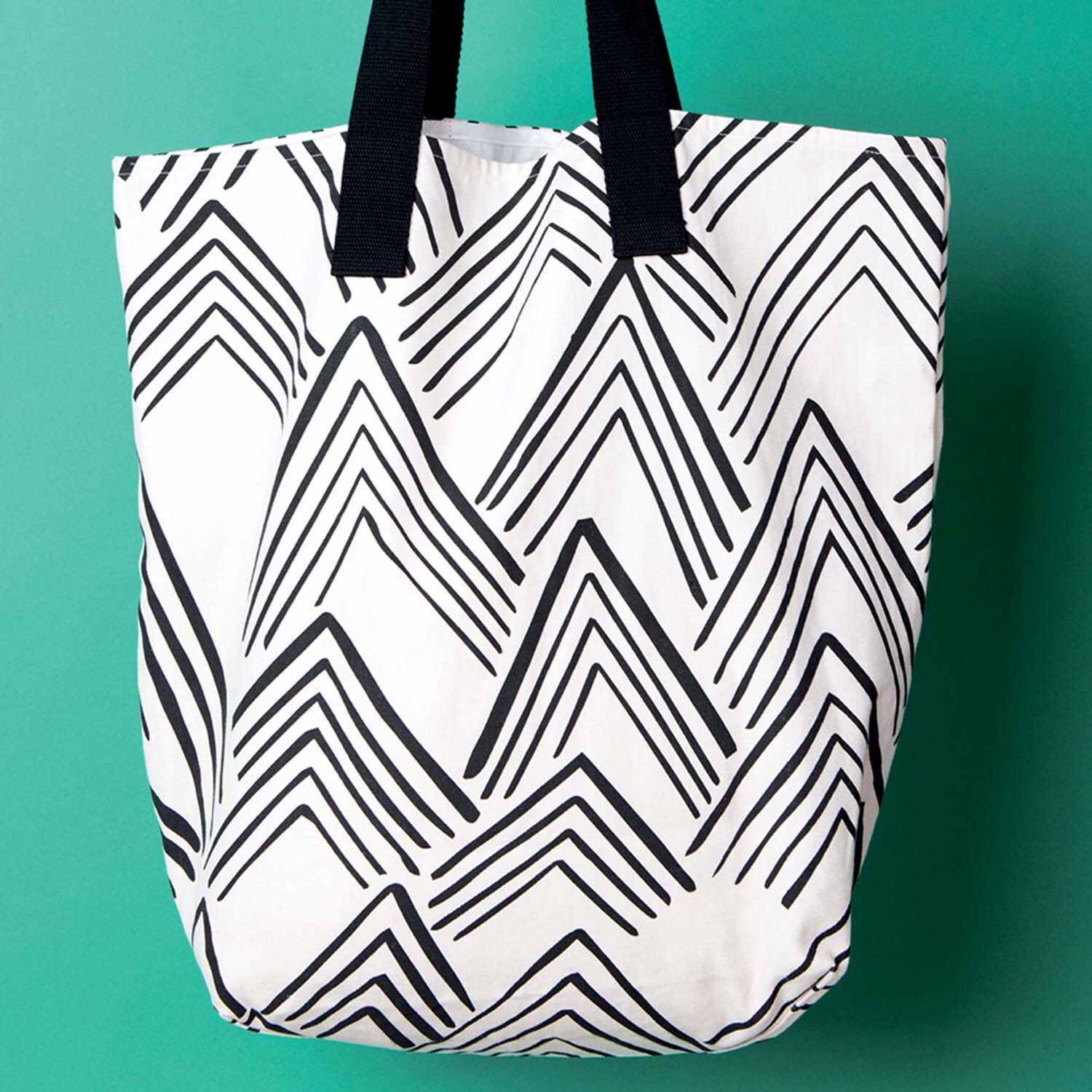 Nähanleitung Canvas-Tasche: Weiße Tasche mit schwarzen Zickzack-Mustern und schwarzen Griffen vor grünem Hintergrund.