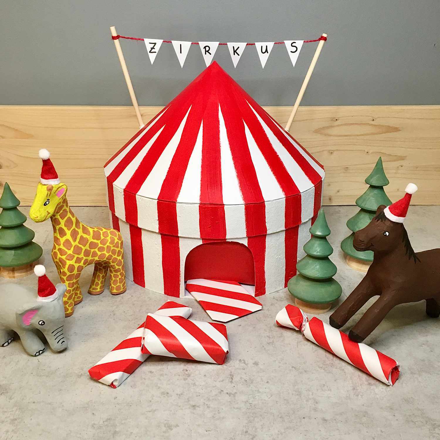 Anleitung Adventskalender Zirkus: Ein rot-weiß gestreiftes Zirkuszelt mit Tieren und Bäumen.