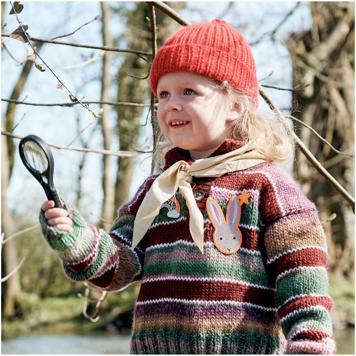 Patches Pfadfinder Hase zum Aufbügeln: Kind mit roter Mütze und Lupe, trägt gestreiften Pullover mit Hasen-Patch von Rico Design.
