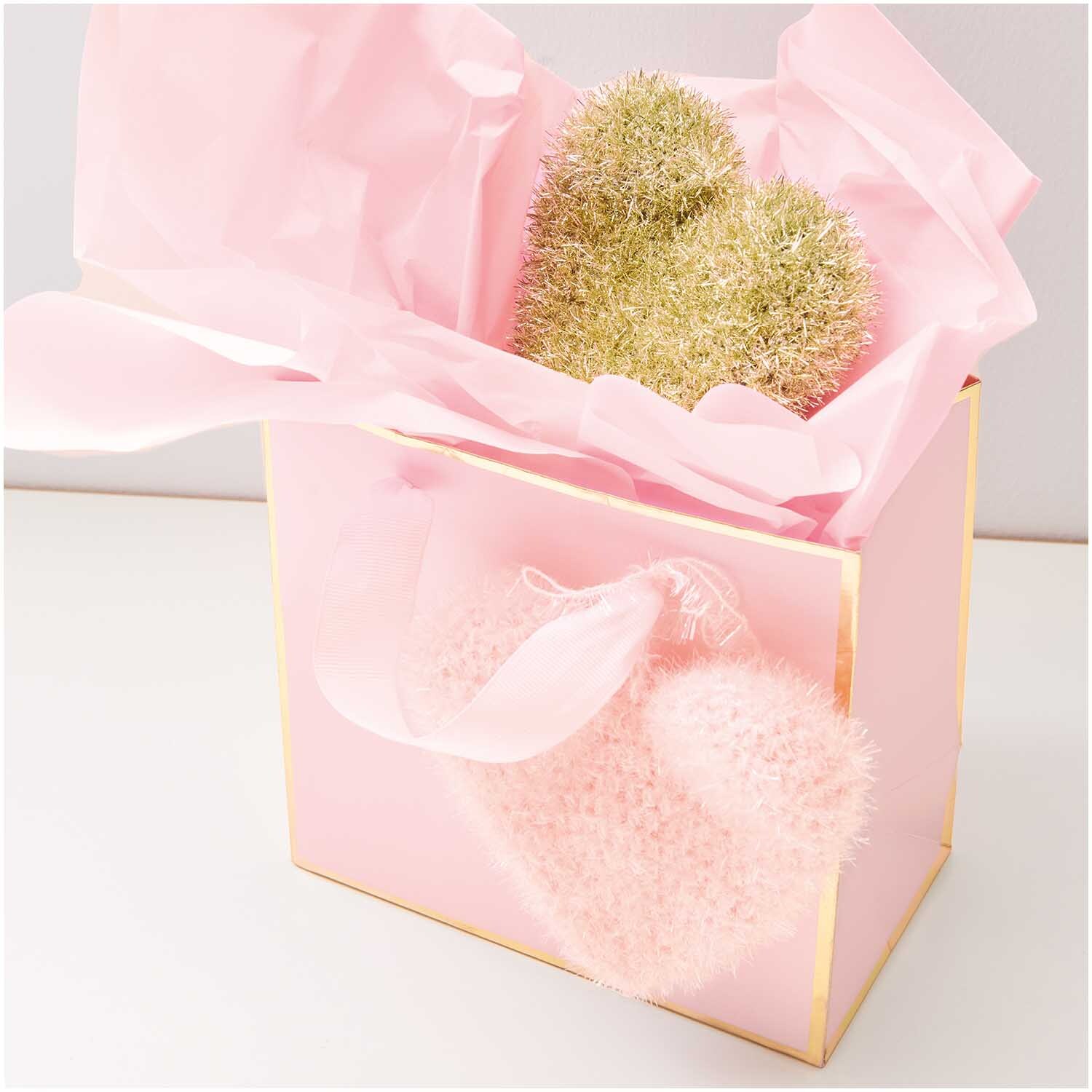 Creative Bubble: Rosa Geschenkbox mit Rico Design Garn, dekoriert mit goldenen und rosa Elementen.
