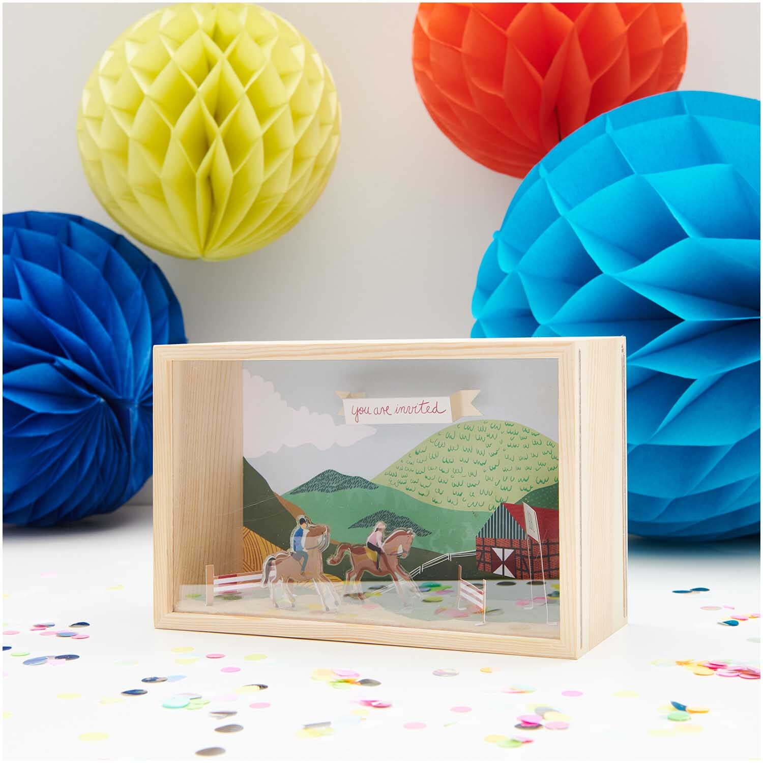 Figurico Objektkasten mit 2 Acrylscheiben zeigt eine bunte Landschaftsszene, umgeben von farbigen Papierbällen.