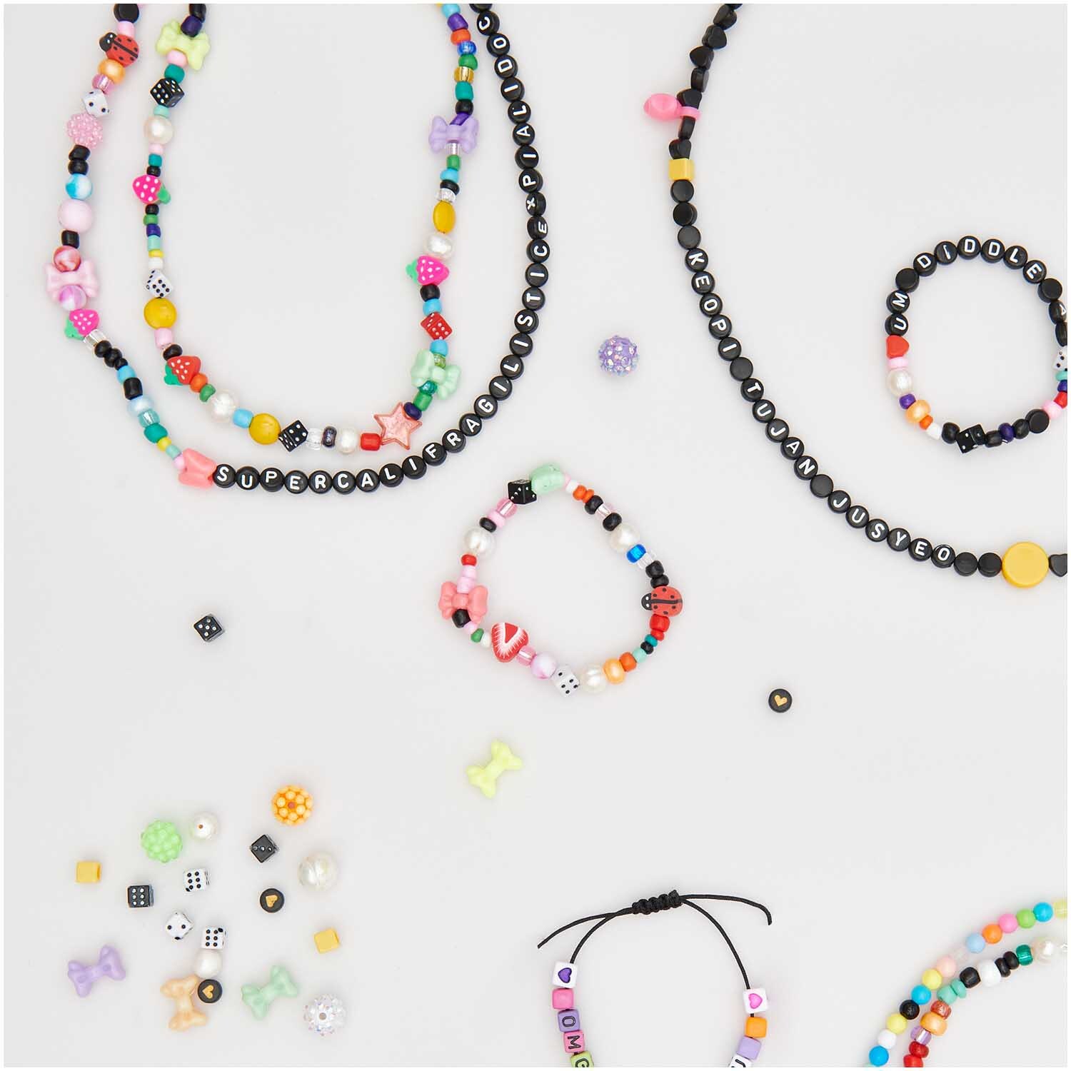 Perlen Buchstaben-Mix rund ca. 165 Stück von Rico Design. Bunte Armbänder und Halsketten mit schwarzen Perlen auf weißem Hintergrund.