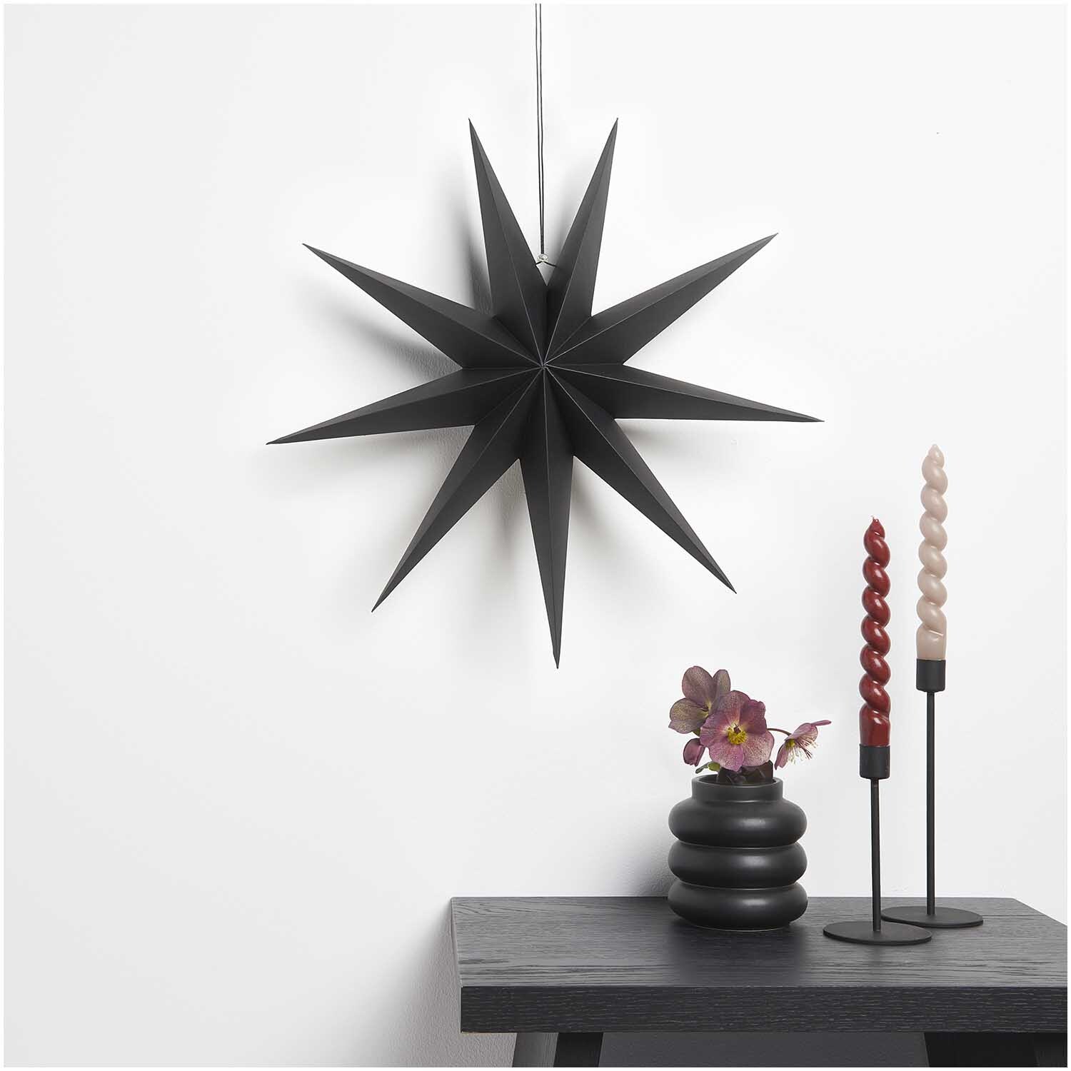 Papierstern auffaltbar 45cm von Rico Design in elegantem Schwarz, dekorativ an der Wand hängend, neben Kerzen und Vase auf einem Tisch.