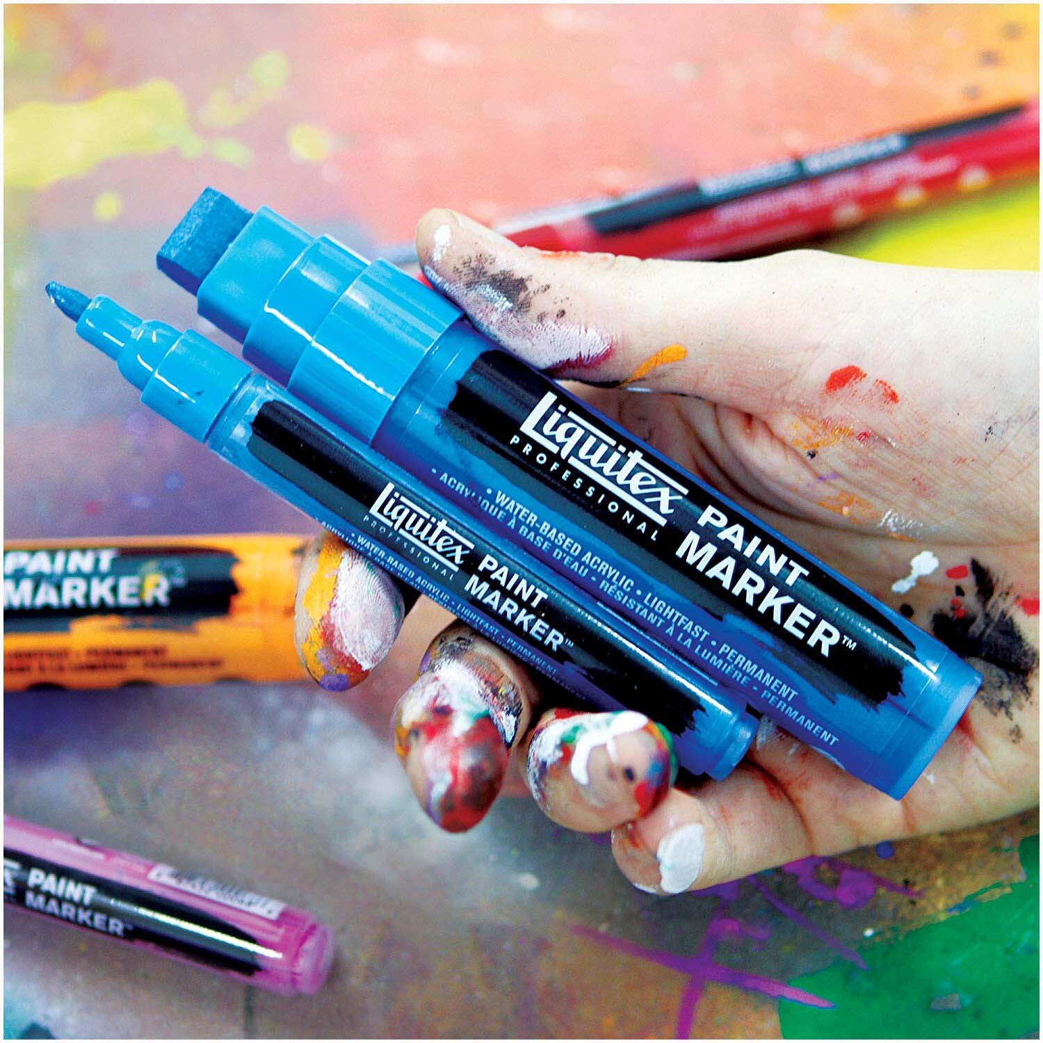 Paint Acryl Marker 2-4mm: Blaue Liquitex Marker in einer bemalten Hand auf bunter Unterlage.