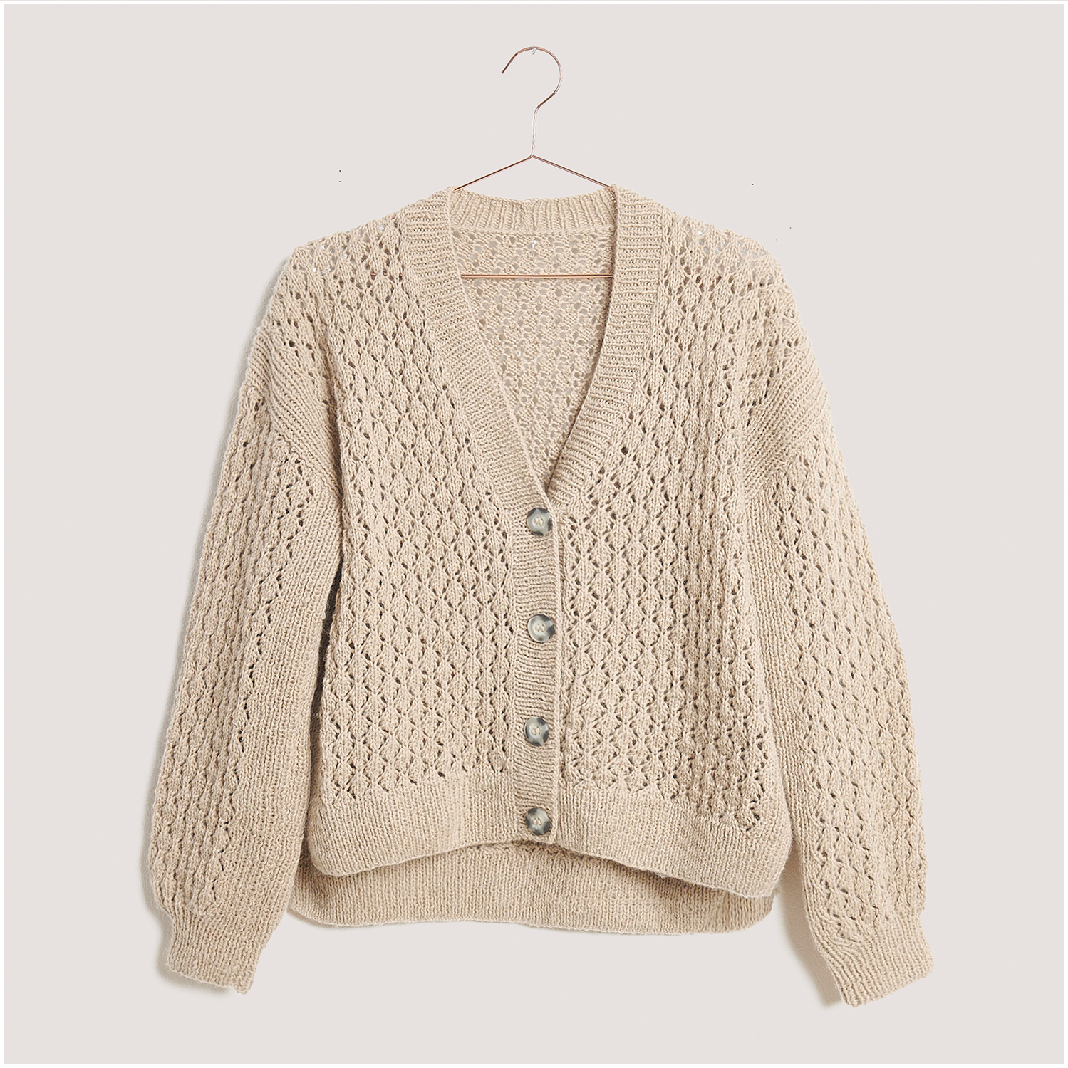 Strickset Jacke Modell 21 aus Lovewool Nr. 18, beige, mit Knopfleiste und V-Ausschnitt, auf einem Kleiderbügel präsentiert.