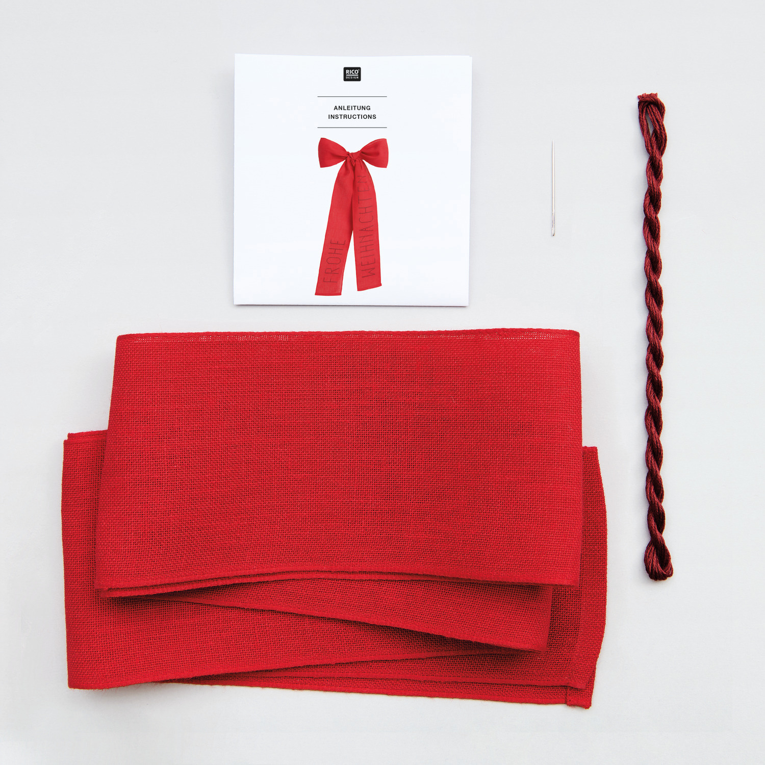 Stickpackung Schleife Frohe Weihnachten von Rico Design zeigt rotes Material, Anleitung und Nadel. Perfekt für festliche Dekorationen.