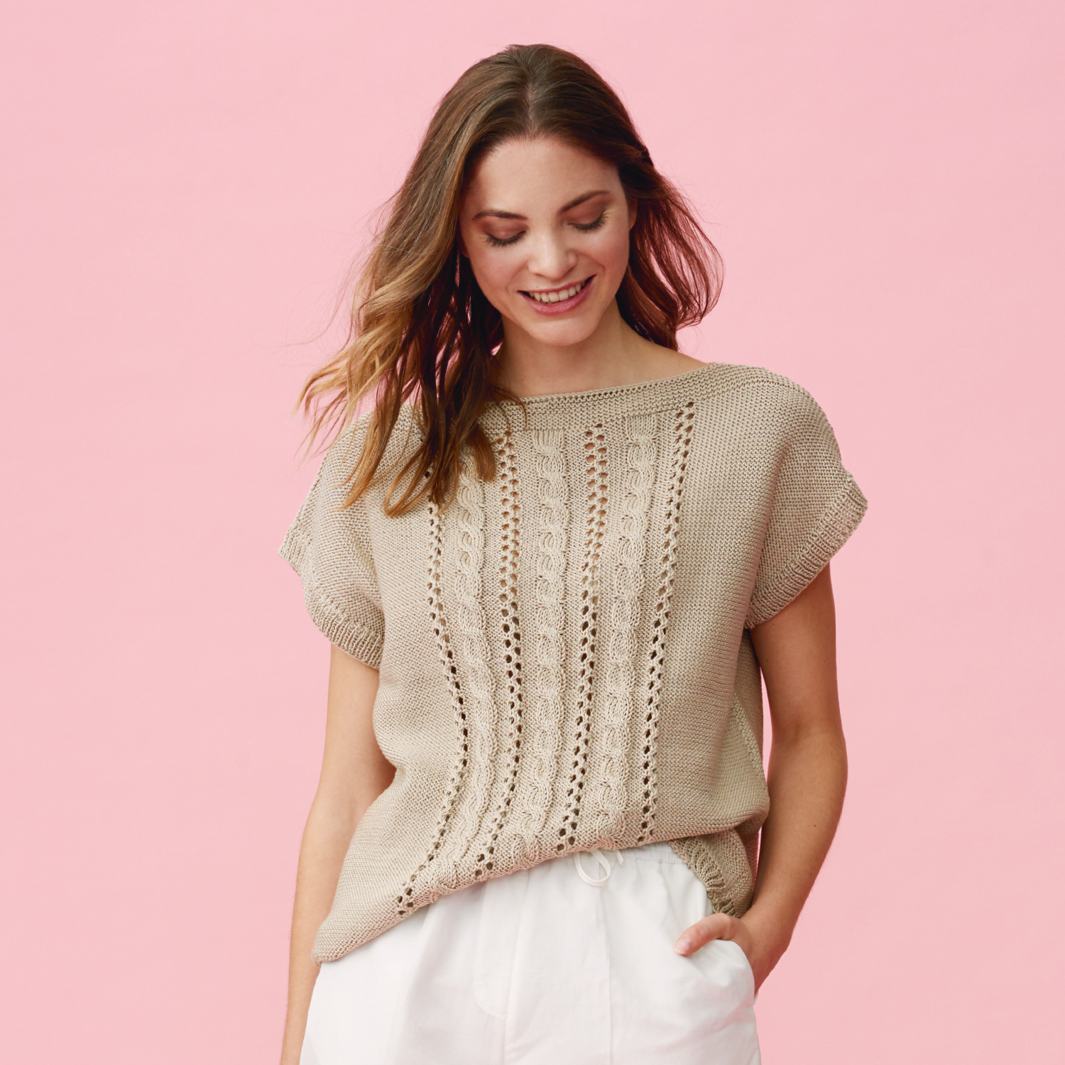 Strickanleitung Leichtes Top aus Mille Fili: Frau trägt ein beige gestricktes Top mit Lochmuster vor rosa Hintergrund.