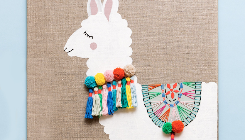 Bastelanleitung Lama auf Leinwand: Ein weißes Lama mit bunten Pompons und dekorativem Sattel auf Leinwand.
