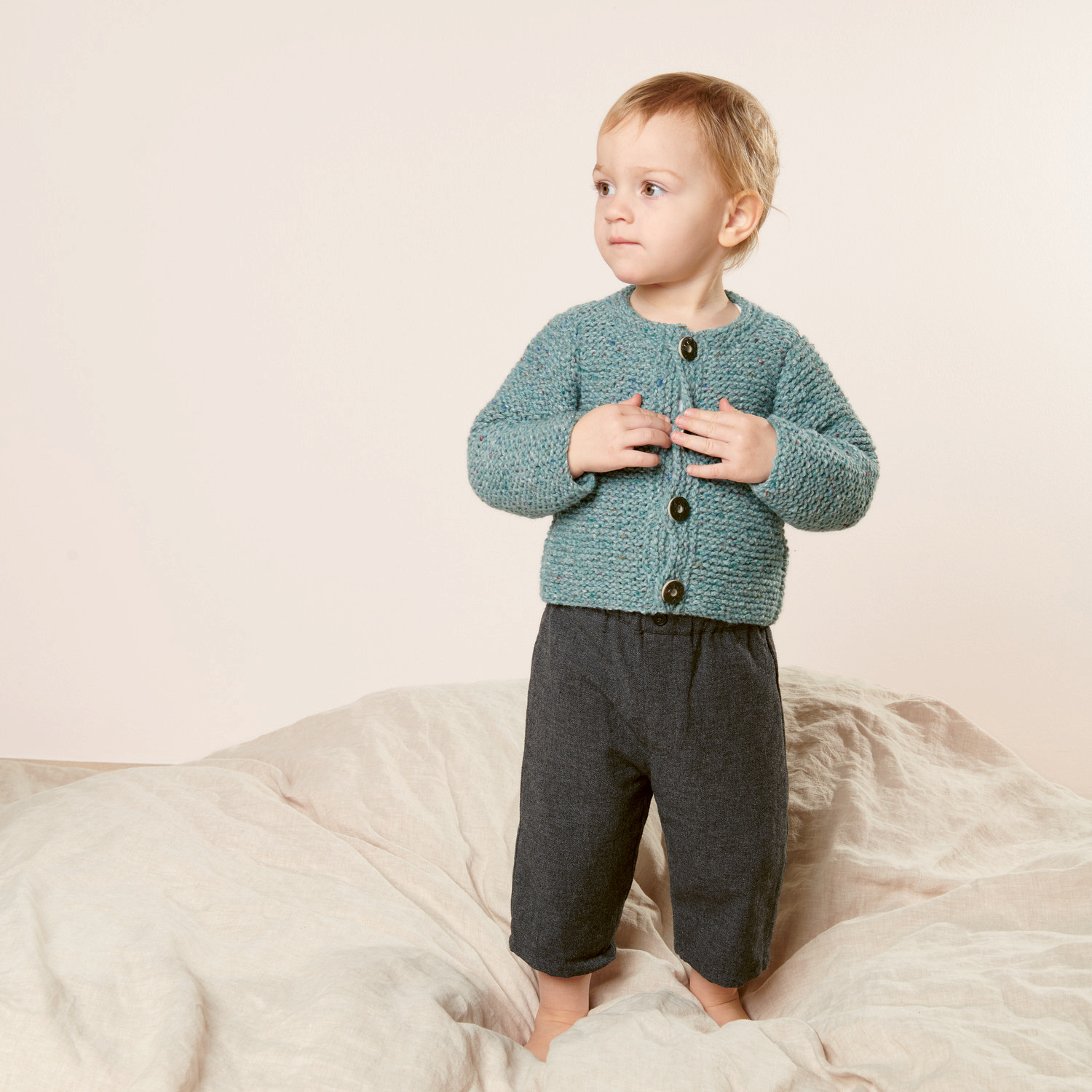 Strickset Babyjanker Modell 16: Kleinkind in grauer Hose und blauer Strickjacke auf hellem Hintergrund.