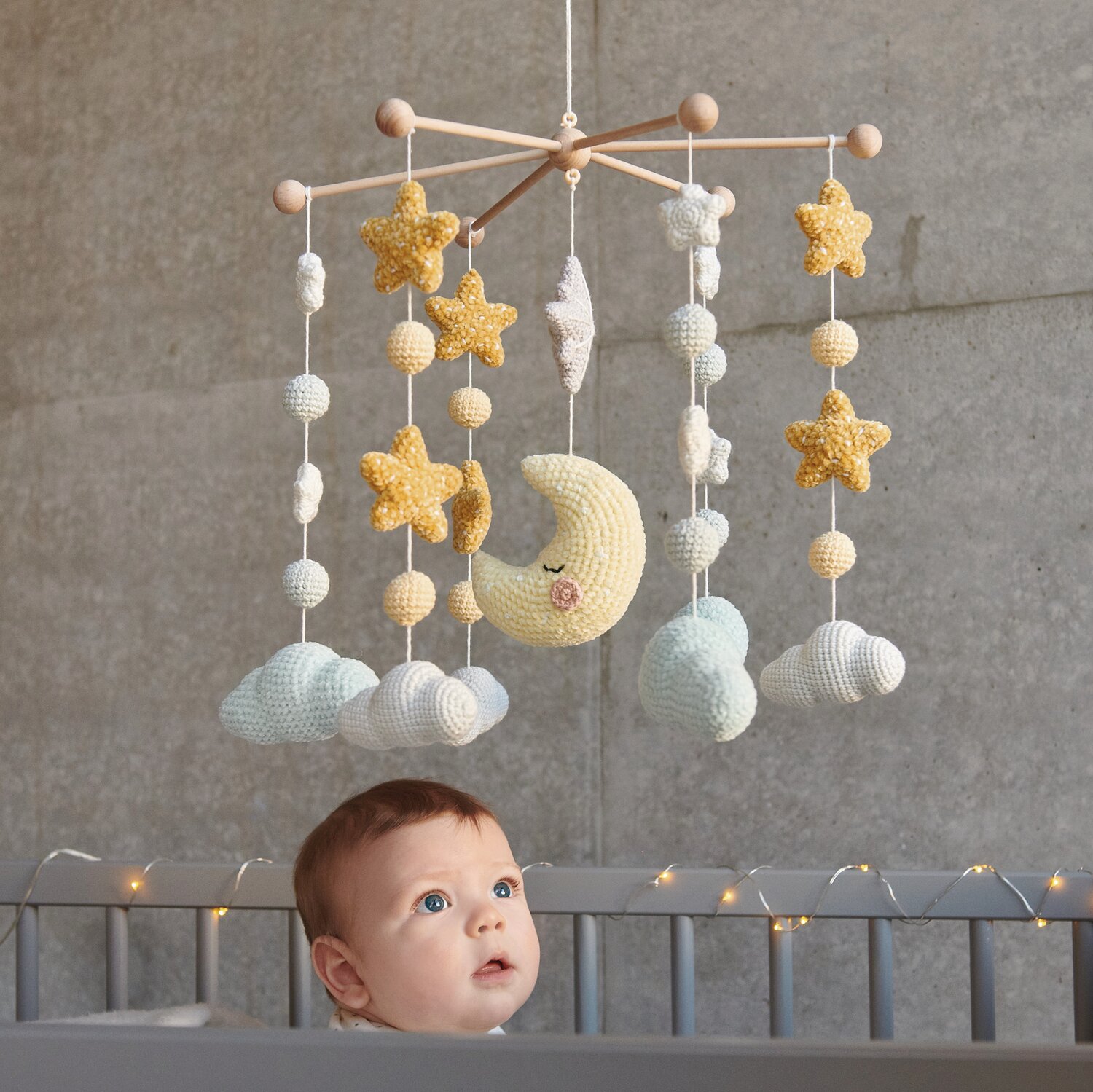 Ricorumi Glow In The Dark: Baby-Mobile mit gelben Sternen, Mond und Wolken über einem Kinderbett.
