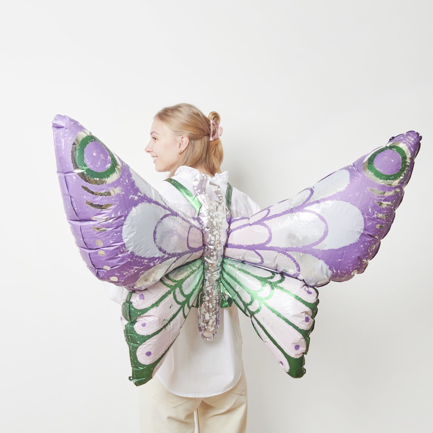 Folienballon Schmetterling zum Umbinden in Lila-Grün von Rico Design, getragen von einer Person.