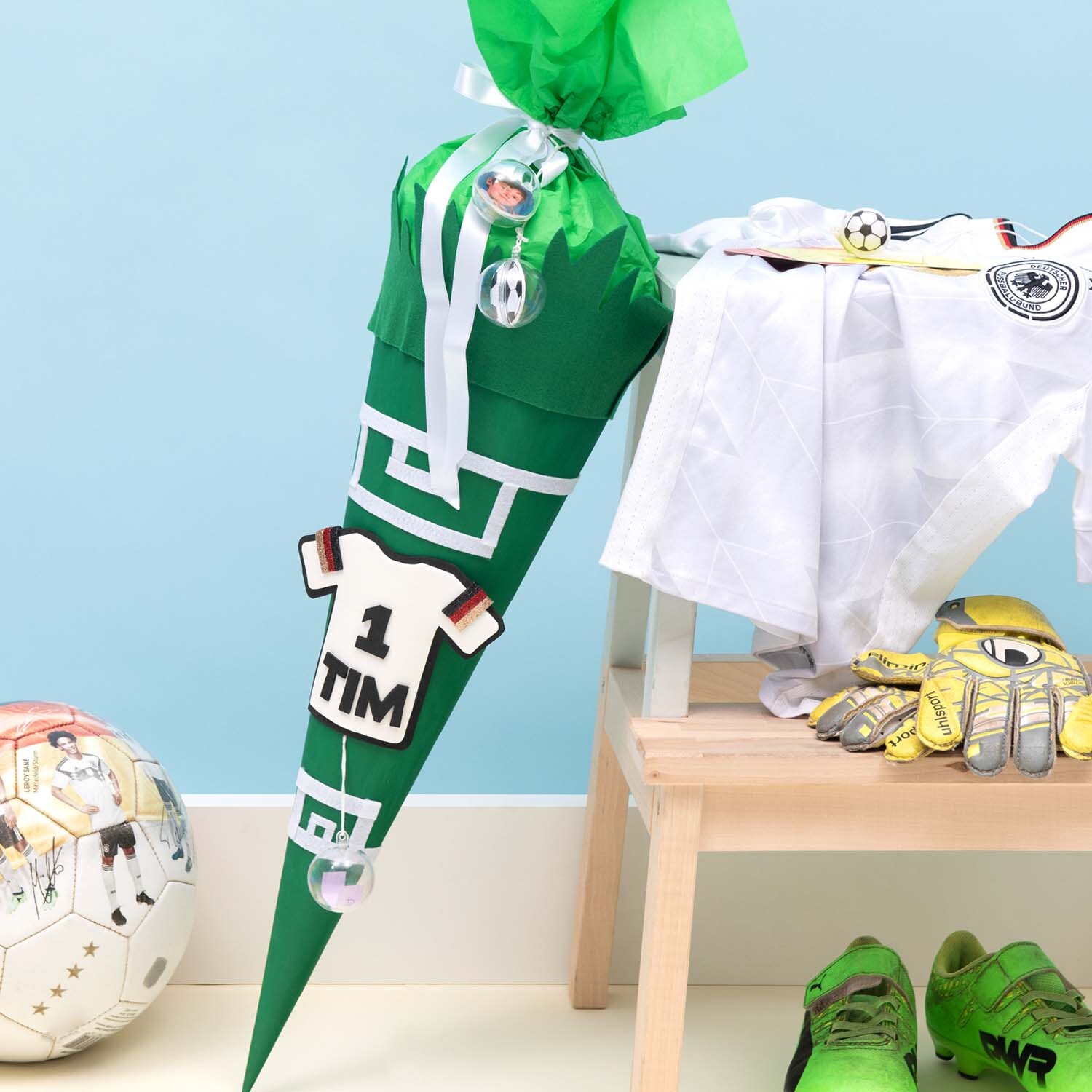 Bastelanleitung Fußball-Schultüte: Grüne Schultüte mit Fußballmotiven, neben Fußballtrikot und Sportschuhen.