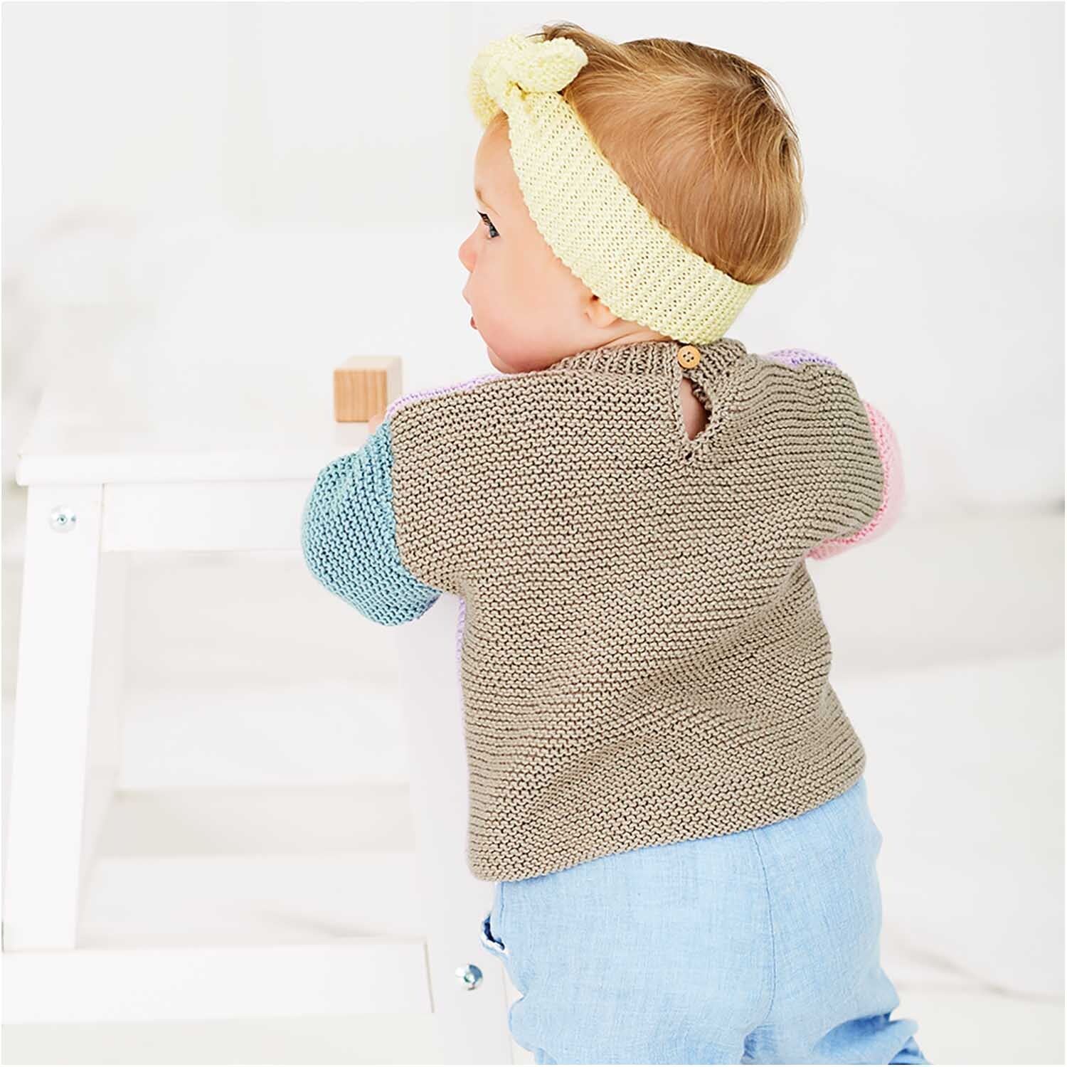 Rico Baby Cotton Soft dk: Ein Baby trägt einen gestrickten Pullover in sanften Farben, passend zu blauer Hose.