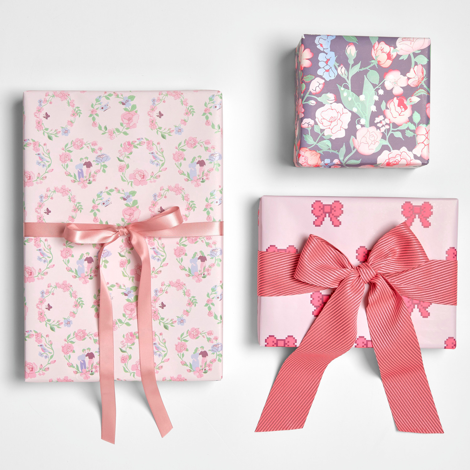 Geschenkpapier Rosen Ranken: Drei Geschenke in zarten Rosatönen mit floralen Mustern und Schleifen.