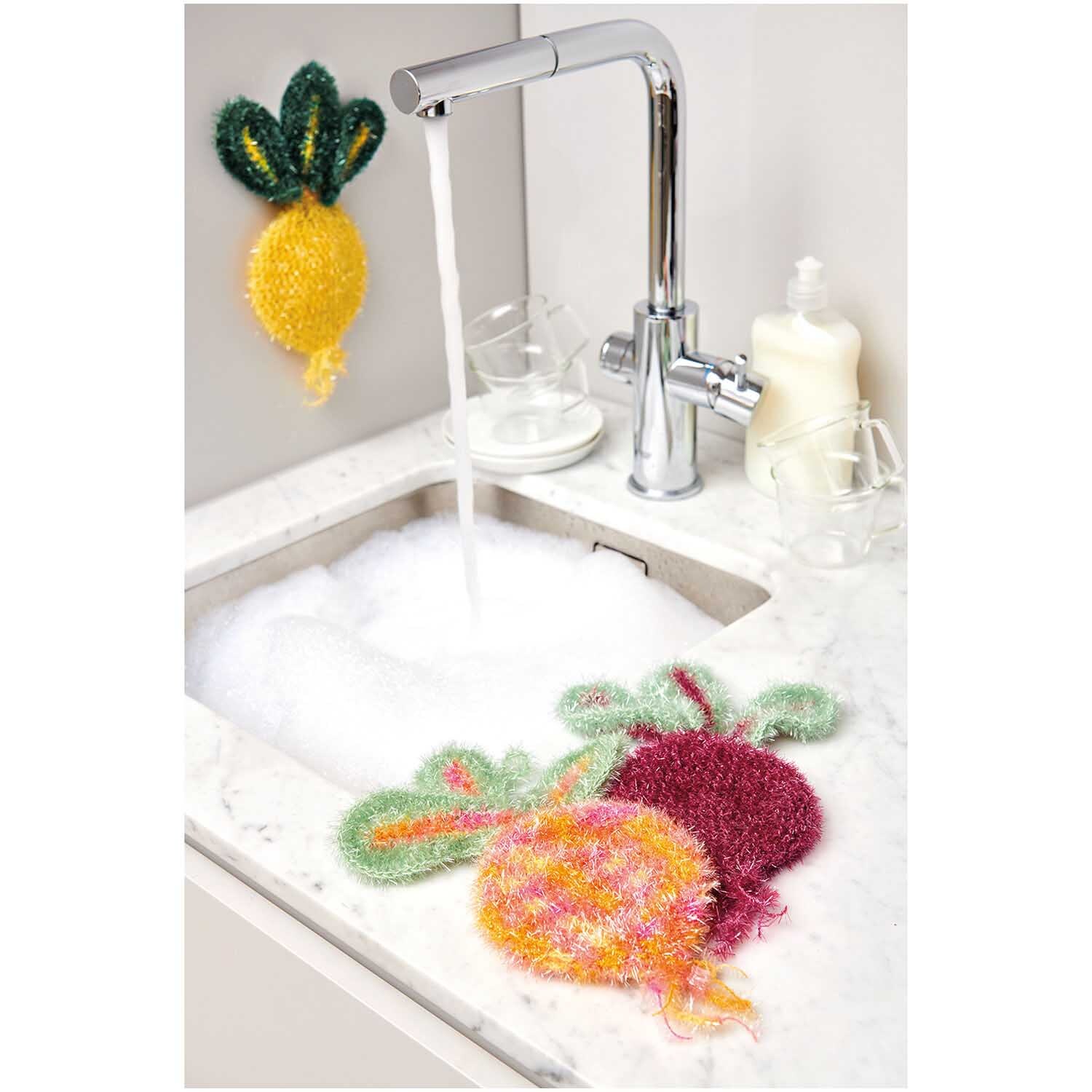 Creative Bubble, Kohl: Bunte Spülschwämme in Gemüseform von Rico Design in einer Küche neben einem Wasserhahn.