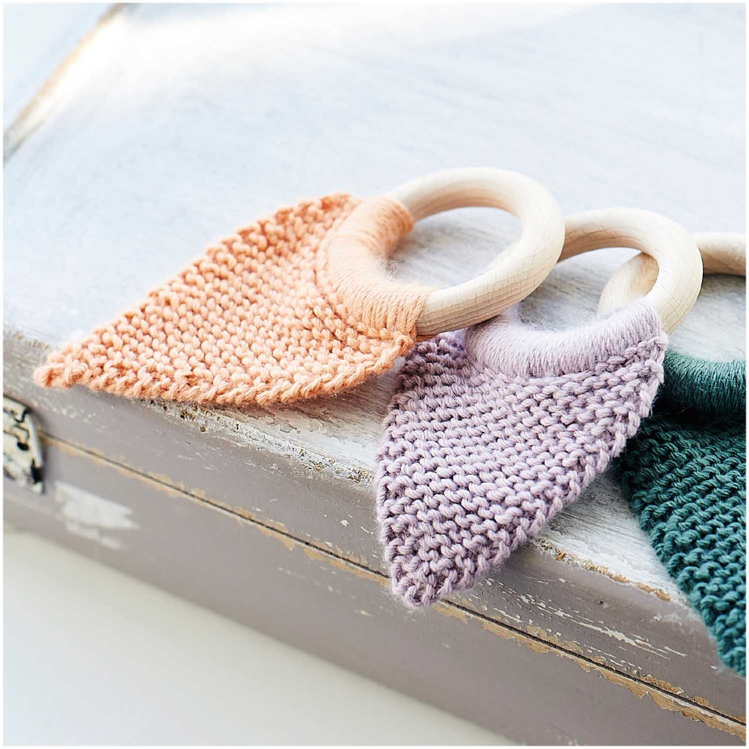 Rico Baby Dream dk uni - A Luxury Touch: Strickringe mit fliederfarbenem Garn auf Holzkiste. Ideal für kreative Handarbeiten.