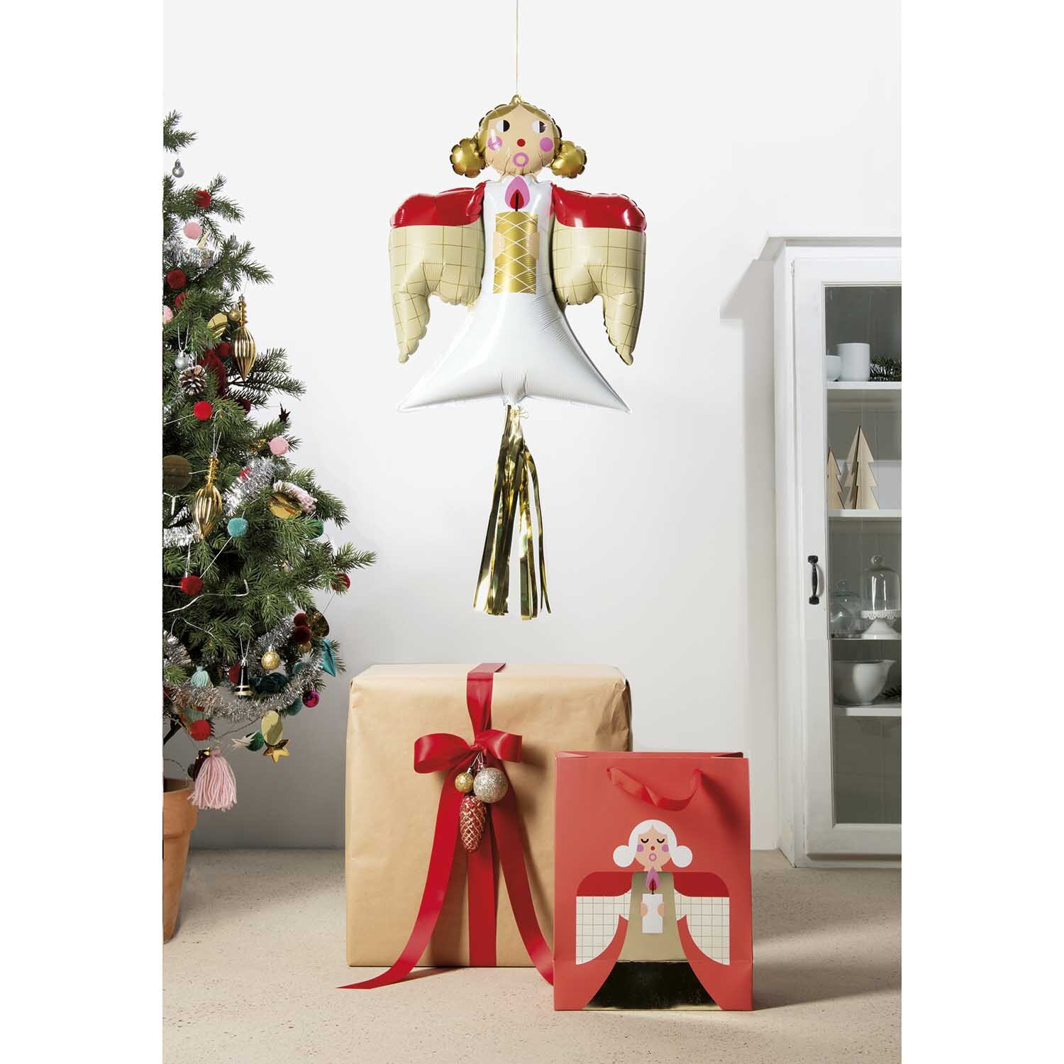 Folienballon Weihnachten Engel schwebt über Geschenken vor einem geschmückten Weihnachtsbaum.