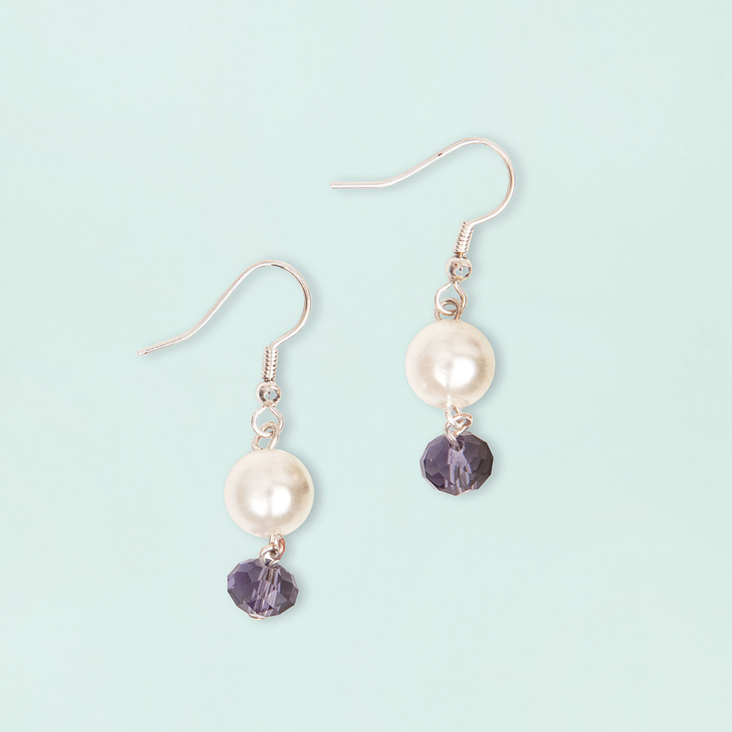 Anleitung Perlenset Fashion Ohrringe basteln: Zwei elegante Ohrringe mit Perlen und violetten Kristallen auf hellblauem Hintergrund.