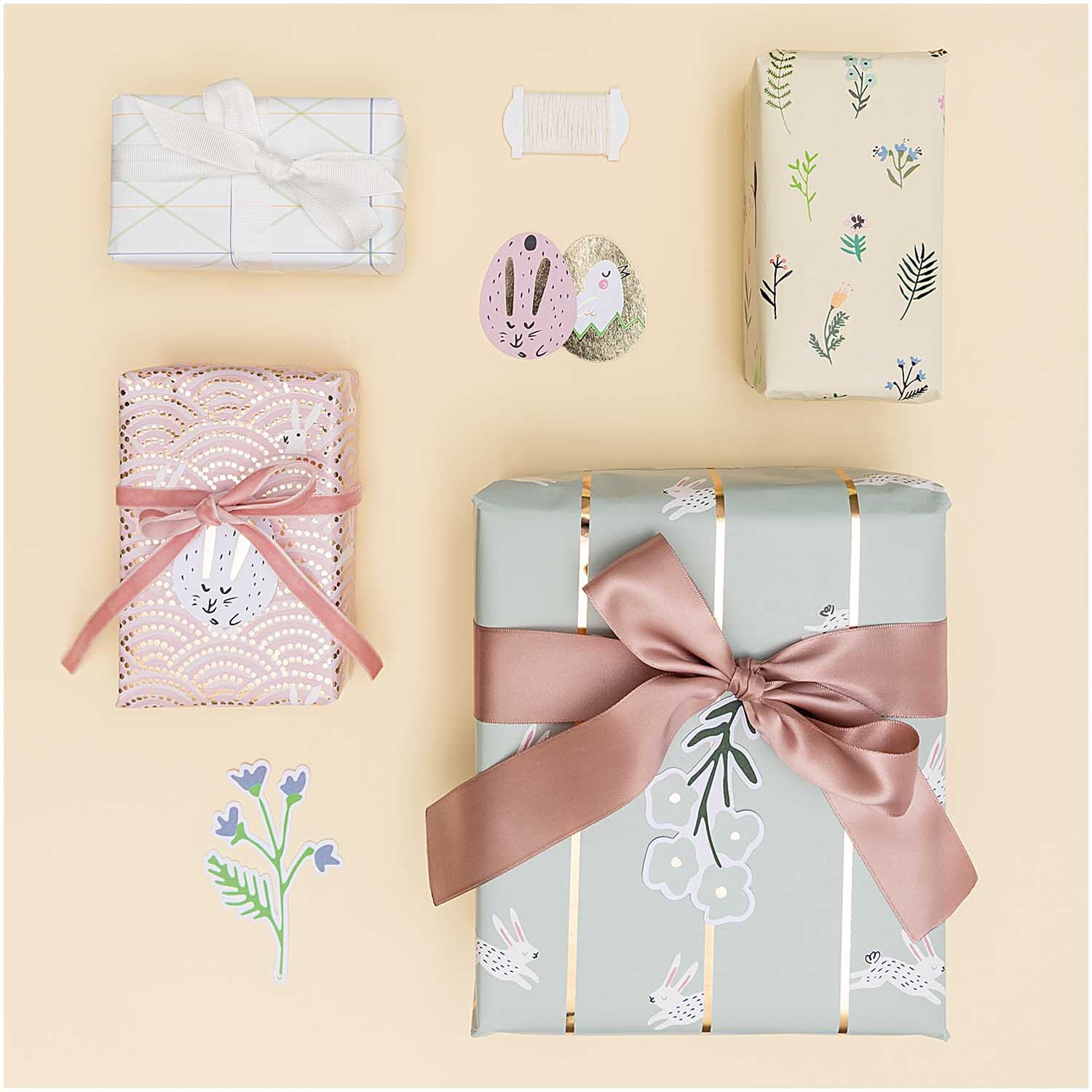 Paper Poetry Geschenkpapier Bunny Hop: Vier Geschenke in pastellfarbenem Papier mit floralen Mustern und rosa Schleifen dekoriert.