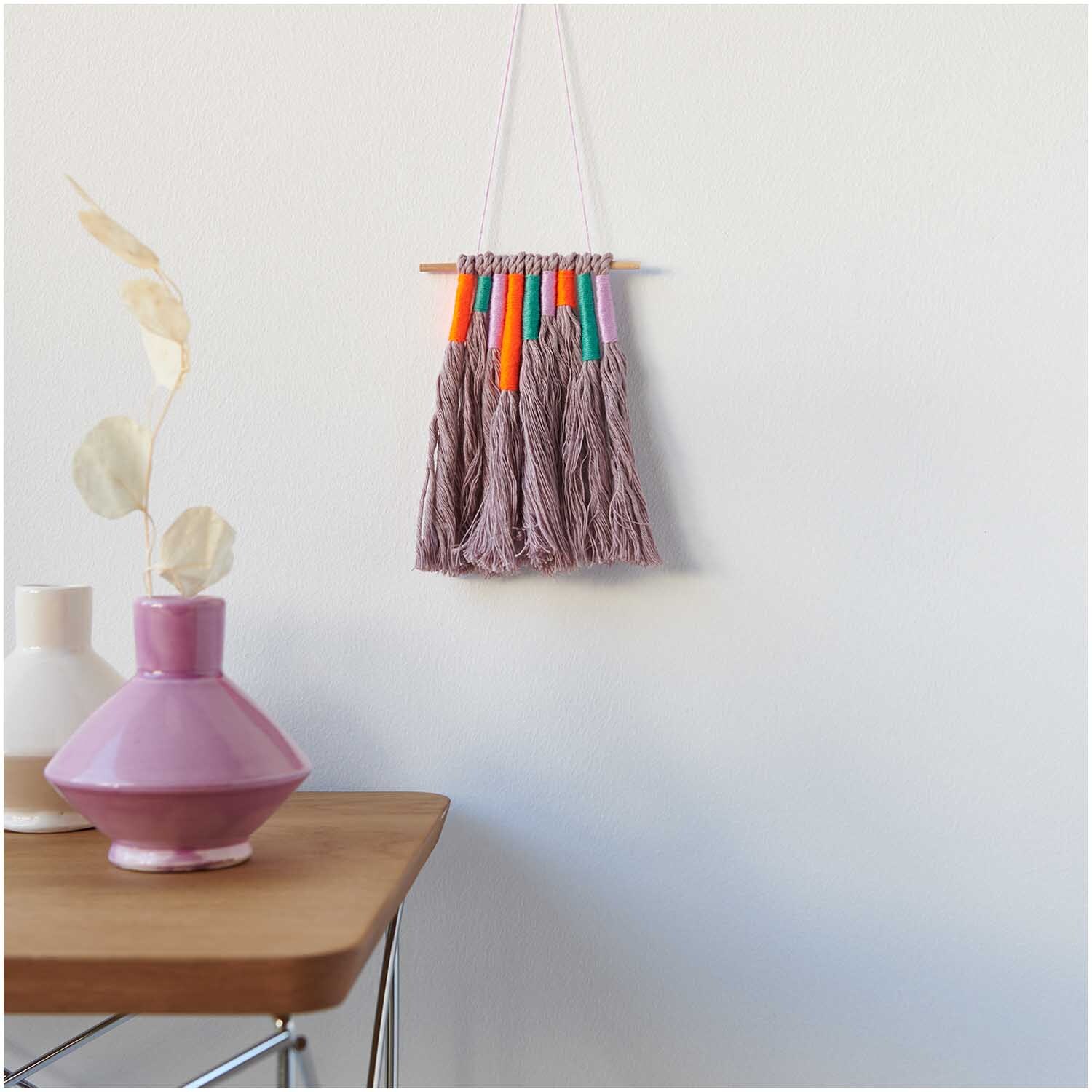 Stickgarn Set Multicolour Fashion, 24-teilig, von Rico Design. Wanddekoration mit bunten Fäden neben Vasen auf einem Tisch.