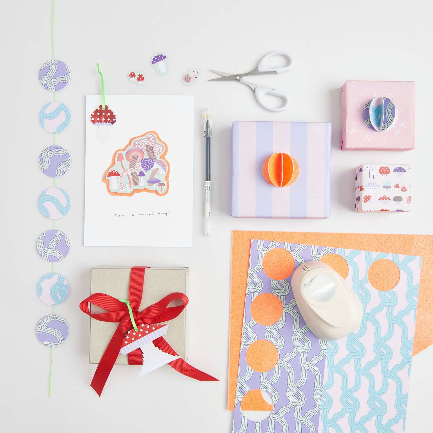 Paper Poetry Motivpapierblock Shrooom mit buntem Bastelzubehör, Geschenkboxen und Schere auf weißem Hintergrund.