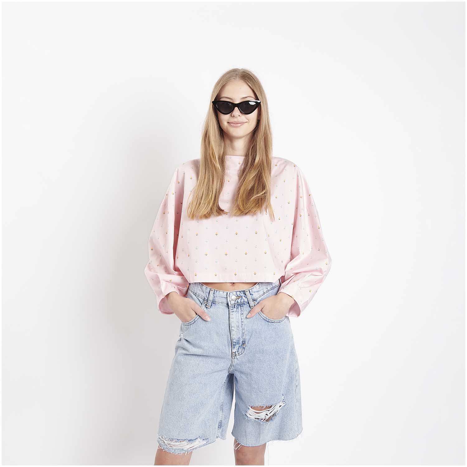 Stoffabschnitt Baumwoll-Popelin Pixel Blumen Rosa: Frau in rosa Oberteil und Jeansshorts, trägt Sonnenbrille. Ideal für modische, sommerliche Outfits.