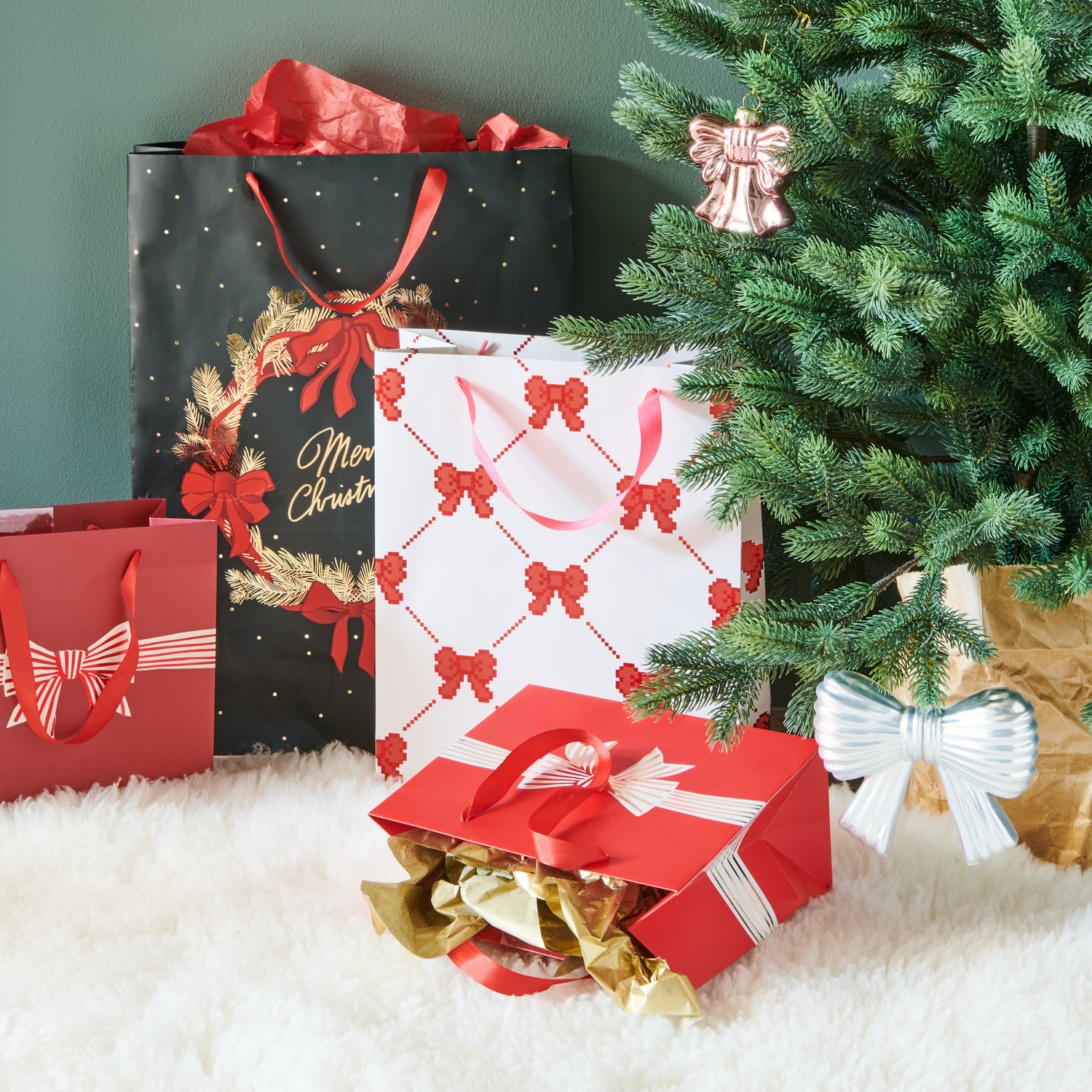 Geschenktüte Pixel Schleifen Creme L von Rico Design unter einem Weihnachtsbaum, umgeben von weiteren festlichen Geschenktüten.