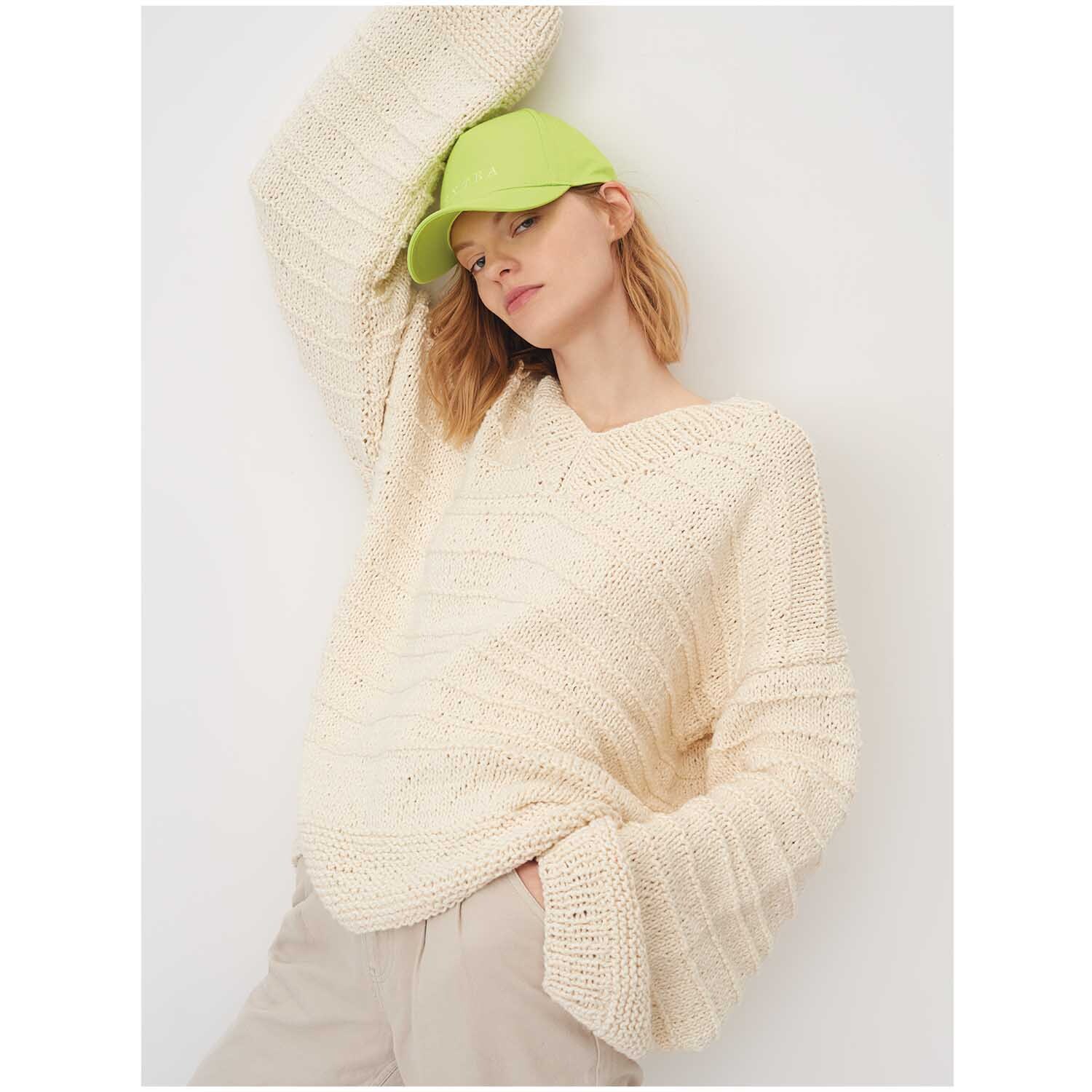 Creative So Cool + So Soft Cotton chunky: Frau in cremefarbenem Strickpullover von Rico Design, lässig mit grüner Kappe posierend.
