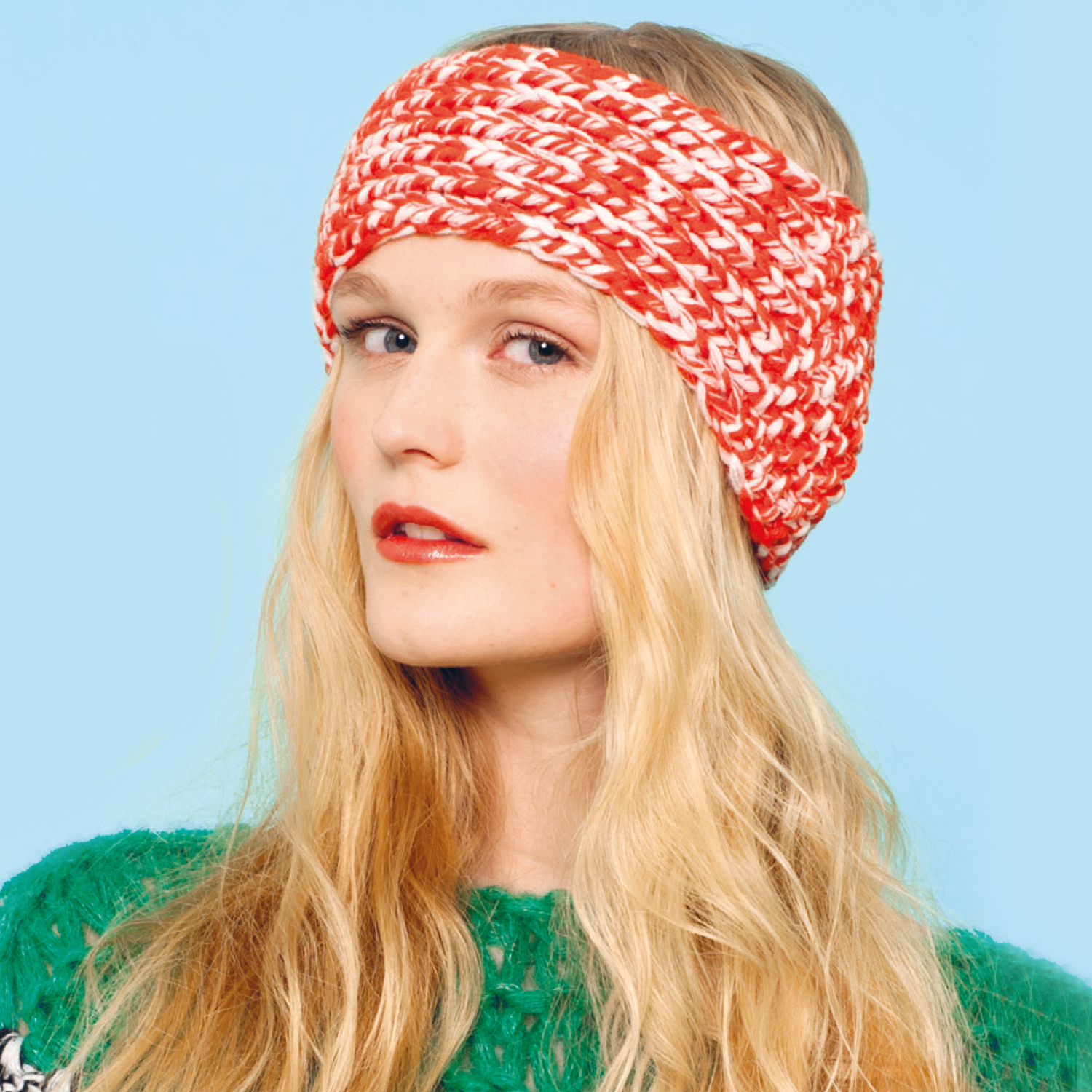 Strickanleitung Stirnband aus Essentials Big Duo: Frau mit rotem Stirnband vor blauem Hintergrund.