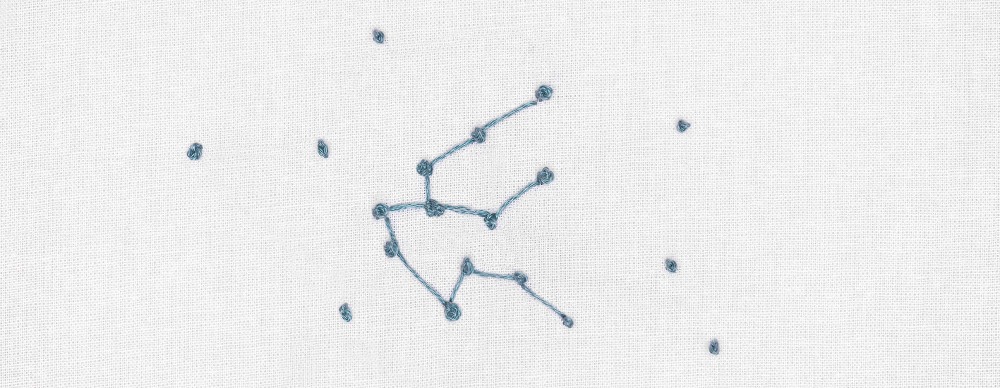 Ein abstraktes Sternenbild ist im Korallenstich auf weißen Stoff gestickt