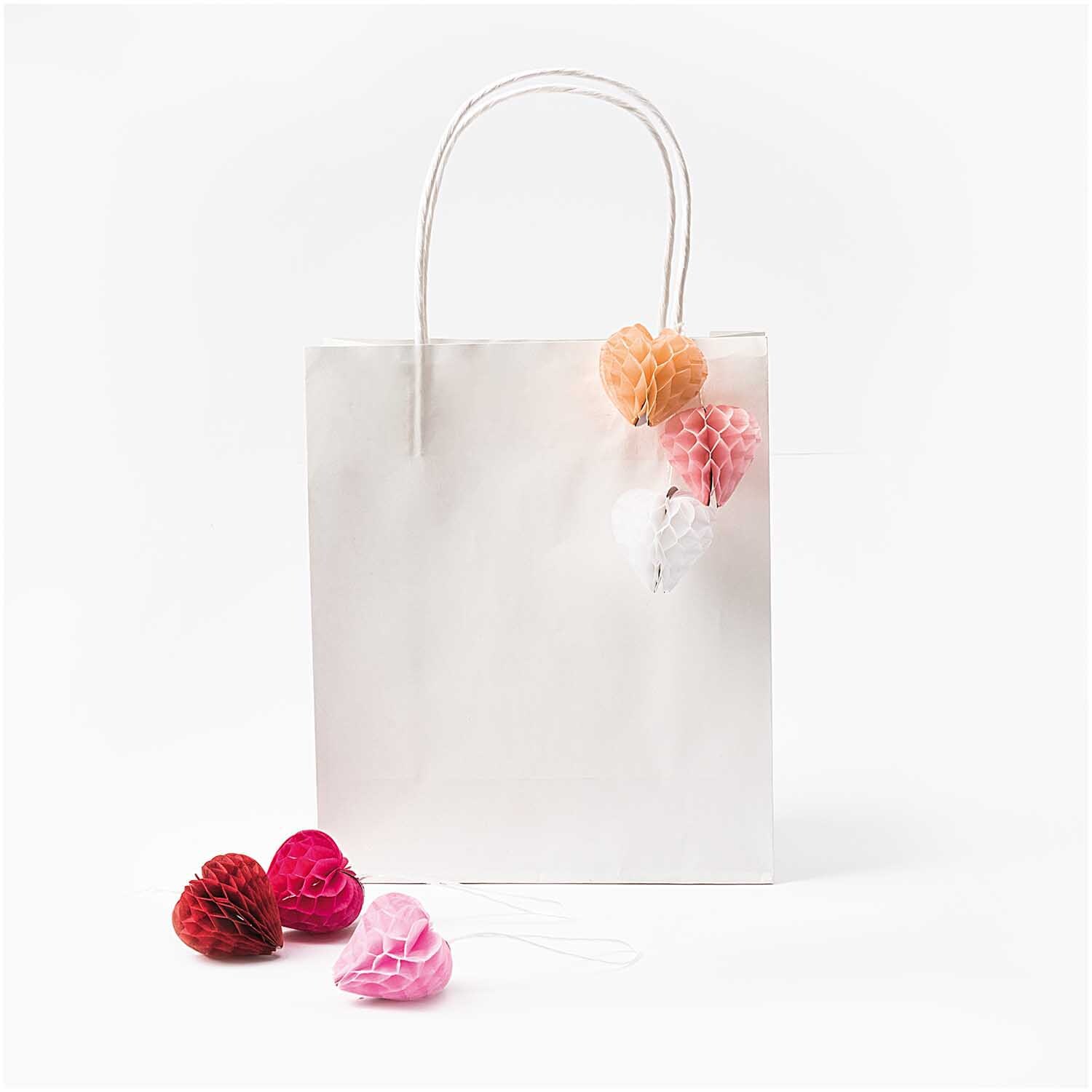 Mini-Wabenbälle Herzen 4cm 6 Stück von Rico Design in verschiedenen Farben an einer weißen Geschenktüte.