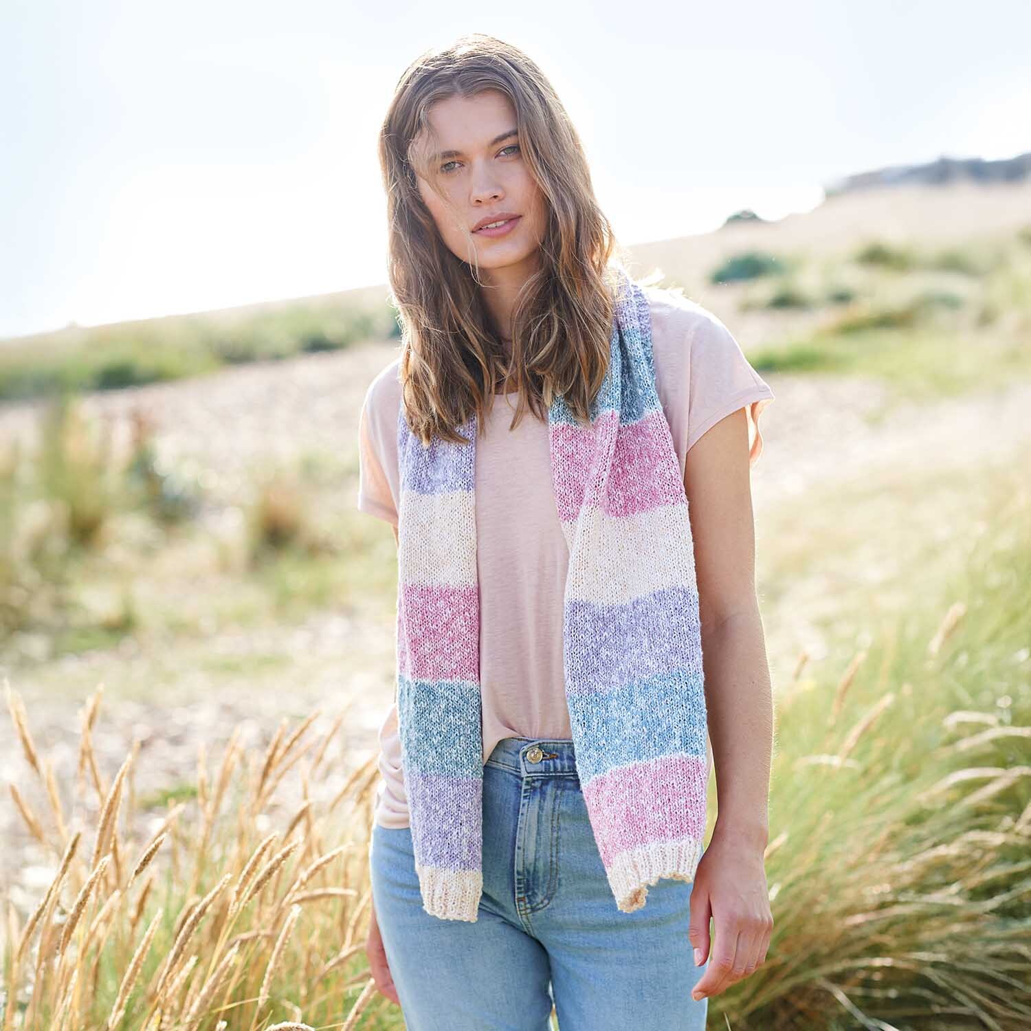Strickanleitung Tuch aus Creative Cotton Stripes dk: Frau trägt pastellfarbenen Schal in Naturkulisse. Ideal für modische, leichte Sommerlooks.