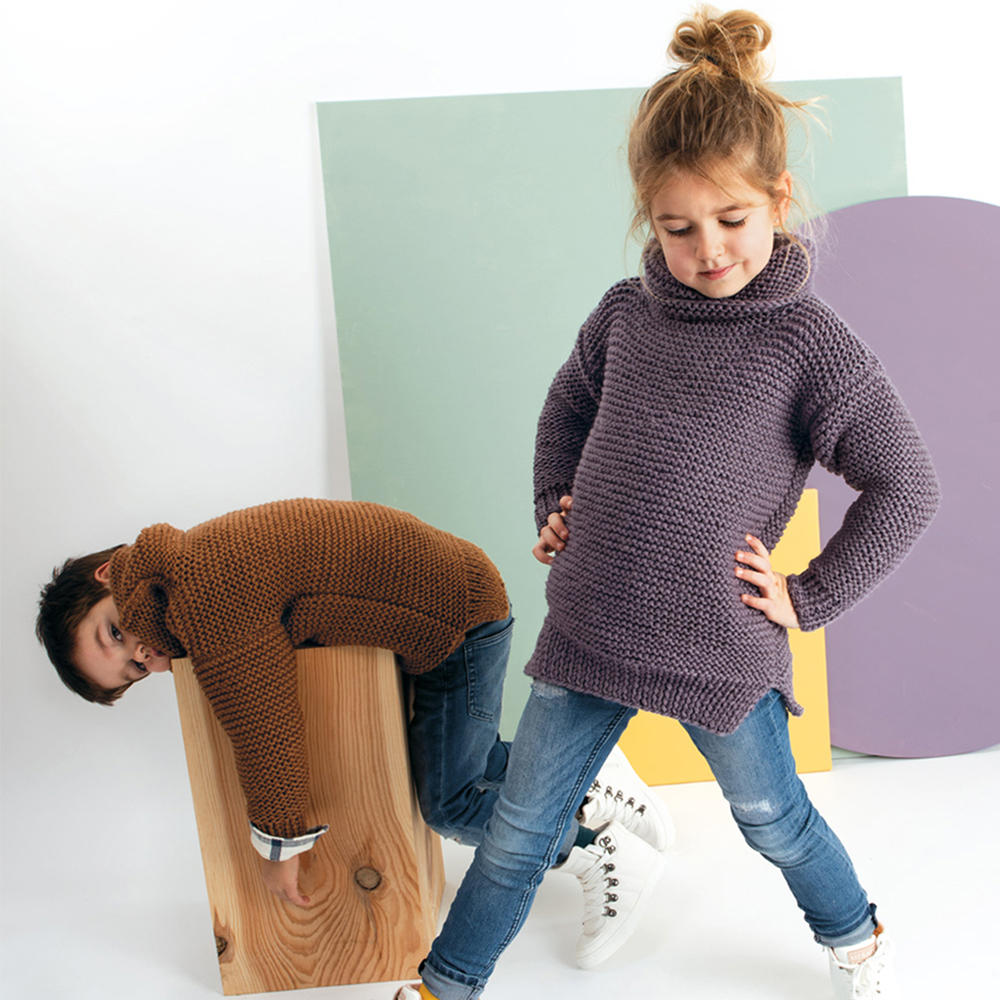 Strickanleitung Rollkragenpullover für Kinder: Zwei Kinder in gestrickten Pullovern, eines in Braun, das andere in Lila, posieren spielerisch.
