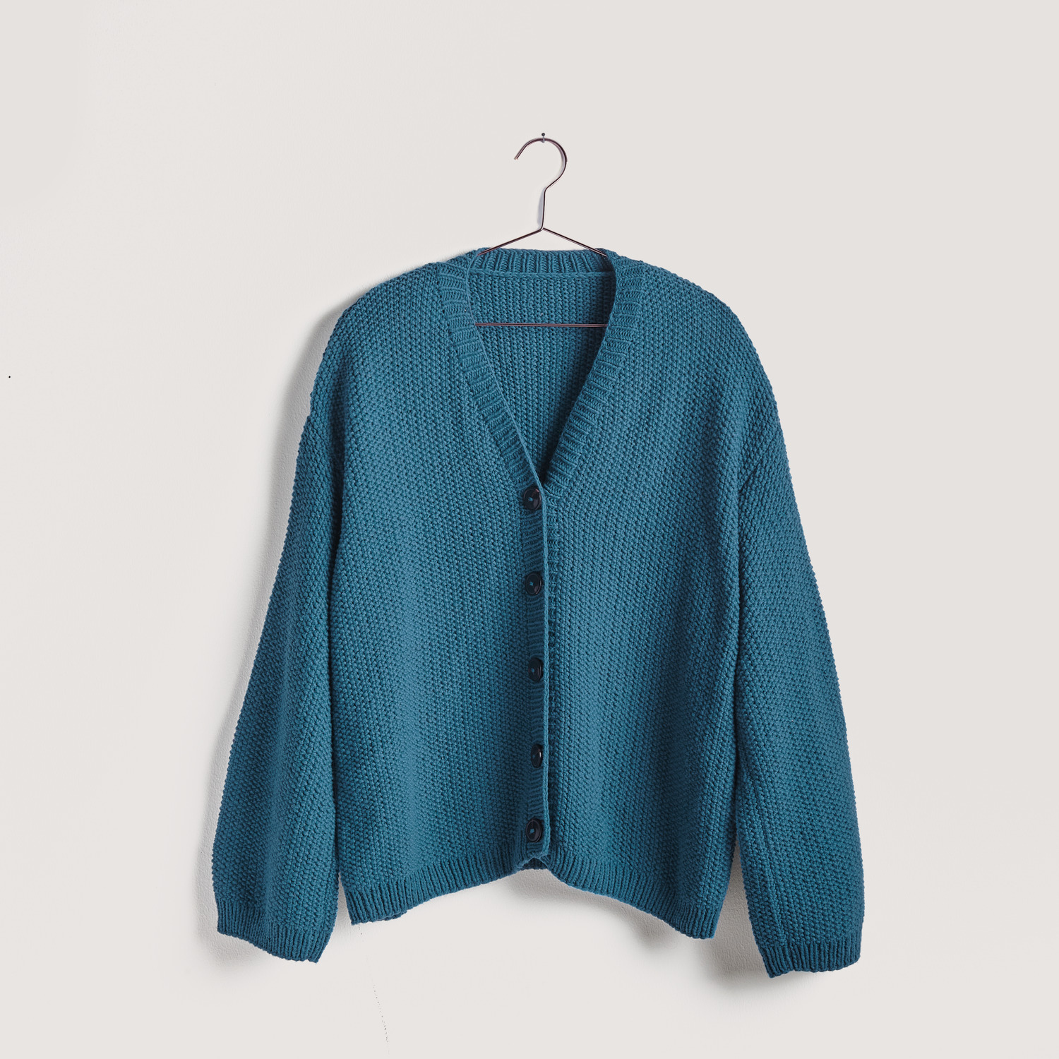 Strickset Cardigan Modell 07 aus Vegan Cashmere von Rico Design in Petrol, hängend an einem Haken.