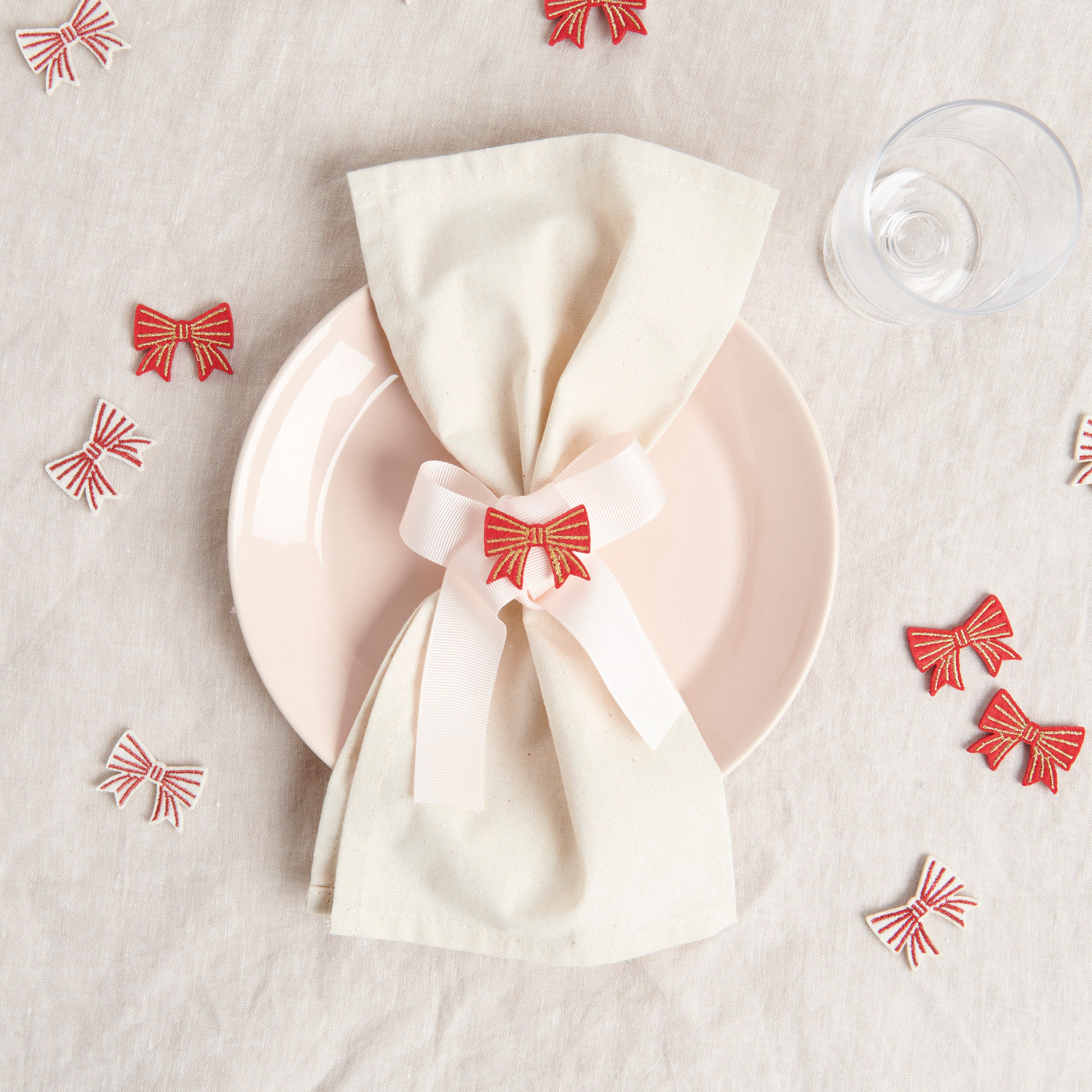 Filzstreu Schleifen dekorieren einen Tisch mit weißem Tuch, rosa Teller und Glas. Rot-goldene Schleifen von Rico Design, 8 Stück.