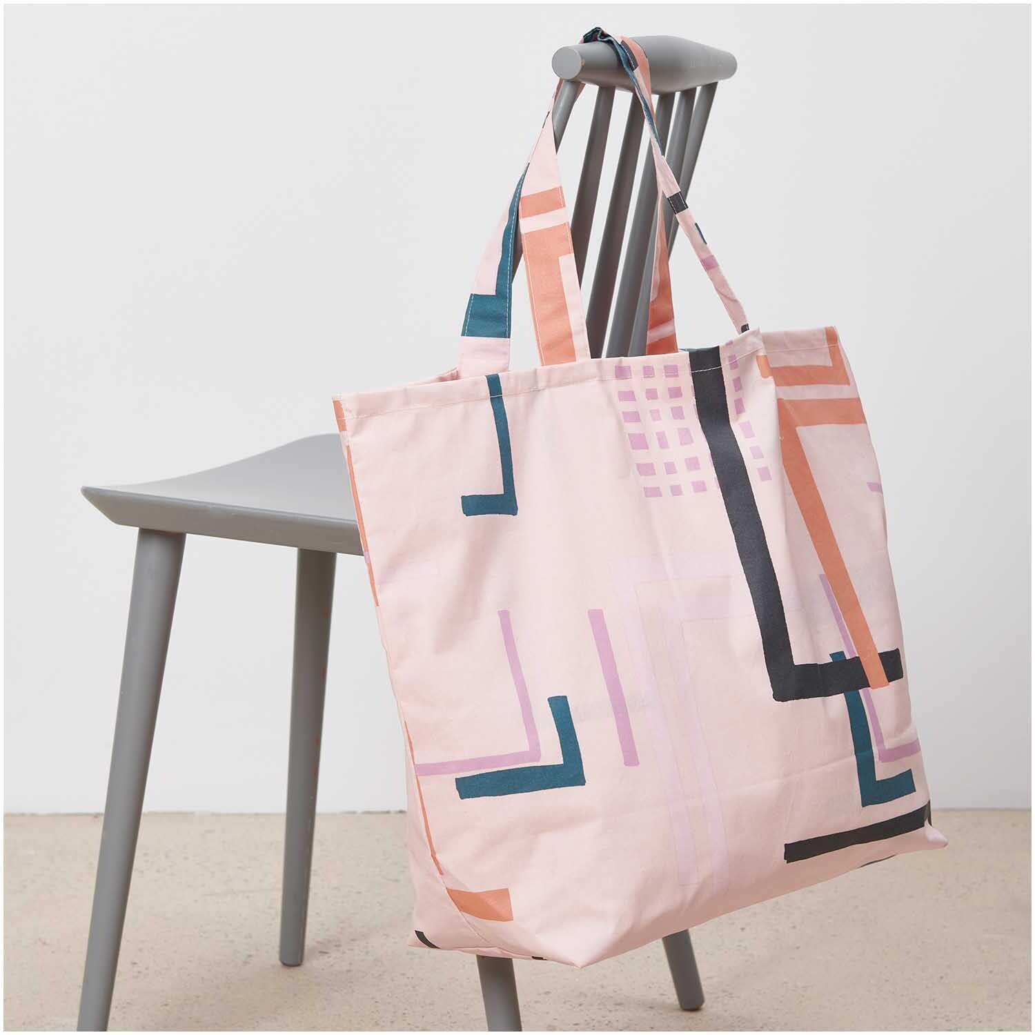 Shopper Okina Hana rosa 41x55x19cm mit geometrischem Muster auf einem grauen Stuhl drapiert.