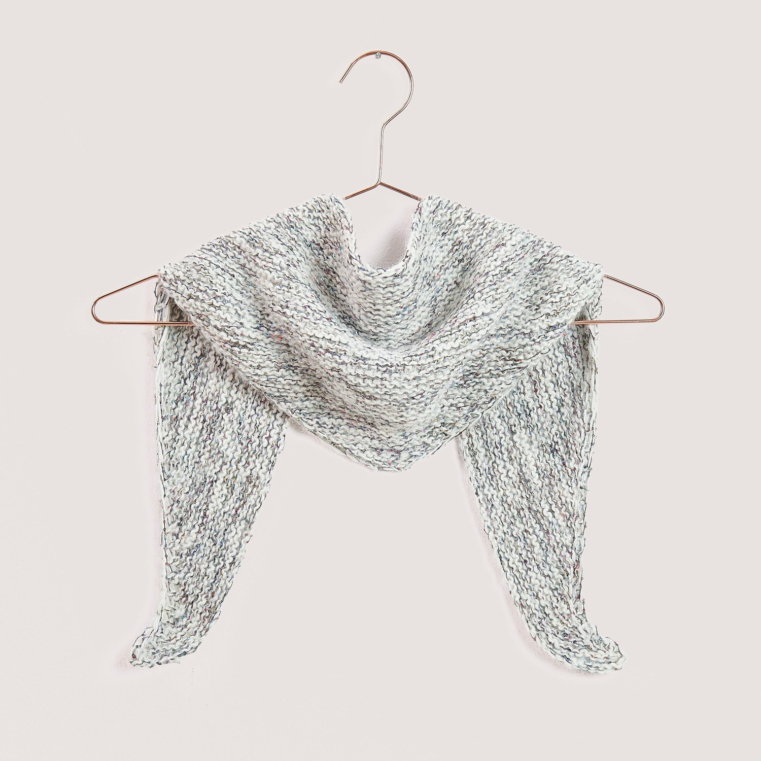 Strickset Mini Dreieckstuch Modell 09b von Rico Design: Elegantes, gestricktes Tuch in neutralen Tönen auf einem Kleiderbügel.